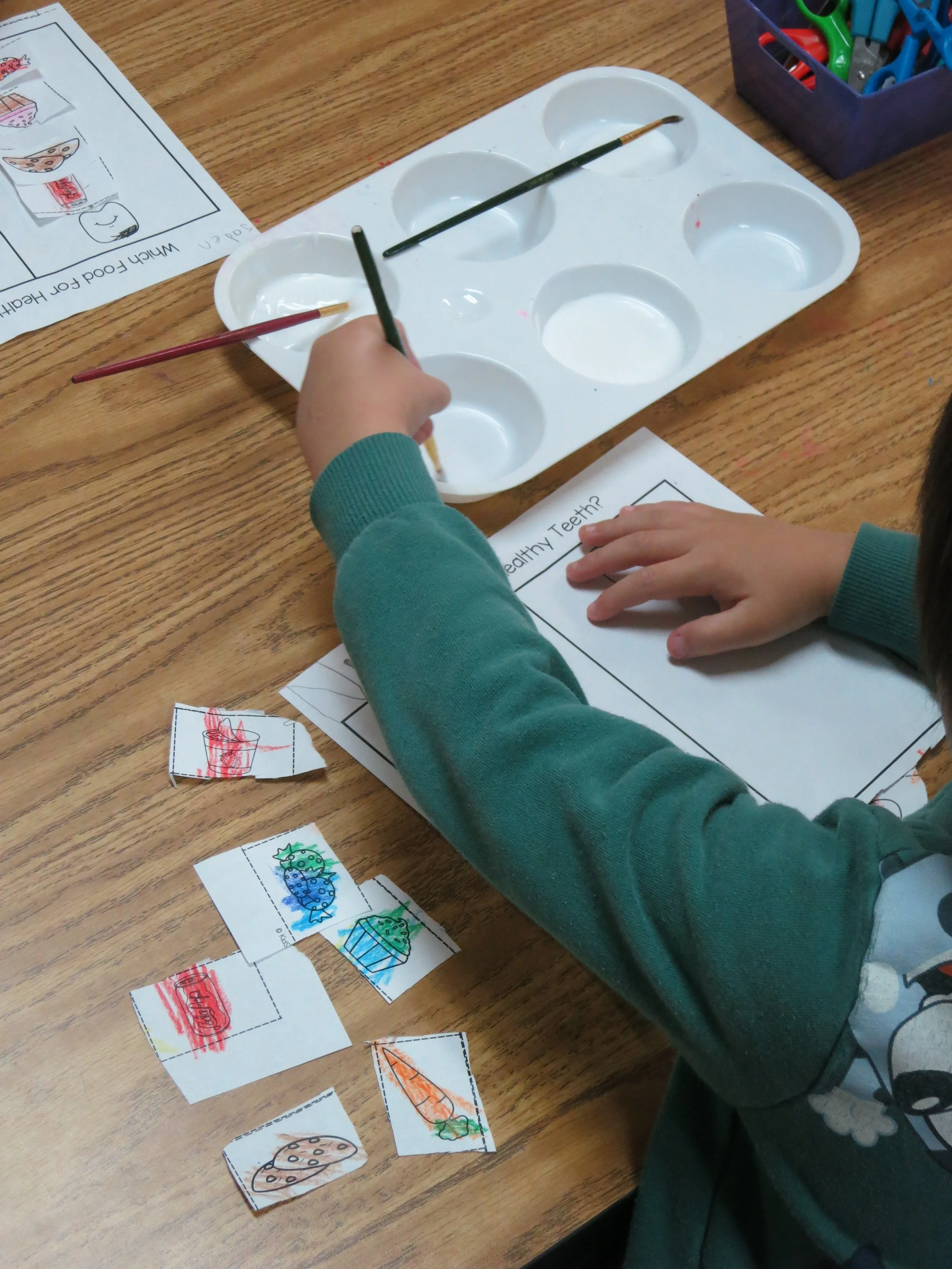 Preschoolers coloring drawings of healthy foods, such as carrots, broccoli, and cookies, on torn pieces of paper. (The Cross Schools of Education - Walnut, CA)