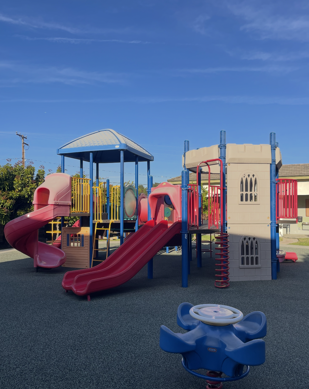Colorful playground structure with slides, climbing areas, and a castle tower, set on a rubberized surface under a clear blue sky. (The Cross Schools of Education - Walnut, CA)