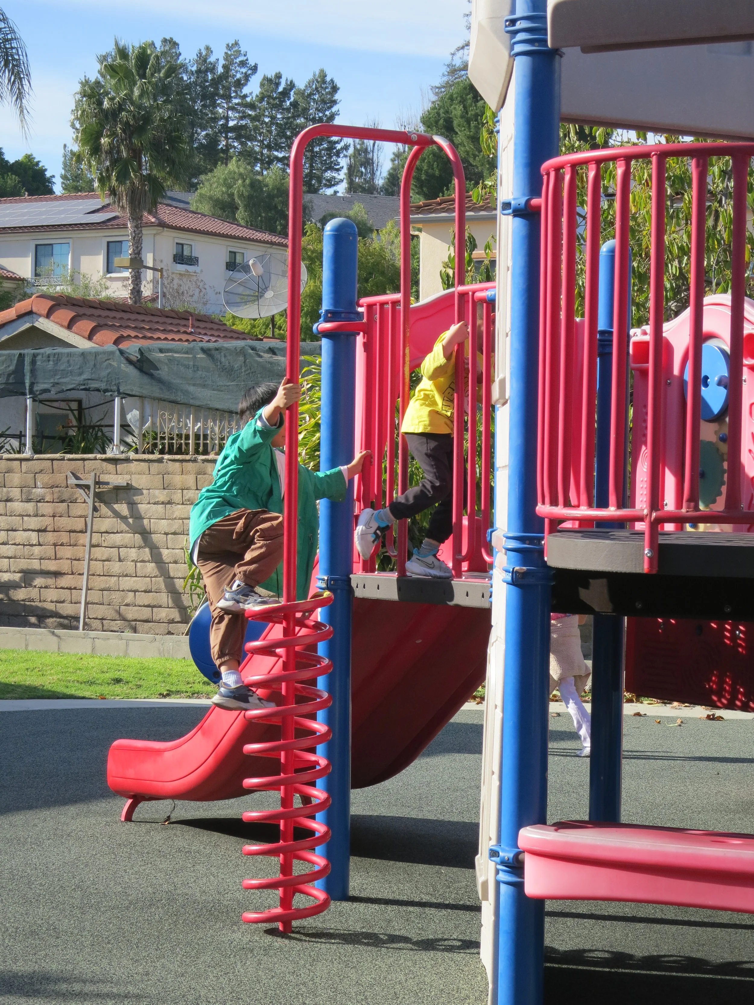 Children playing on colorful playground equipment with a slide and climbing structures outdoors. (The Cross Schools of Education - Walnut, CA)