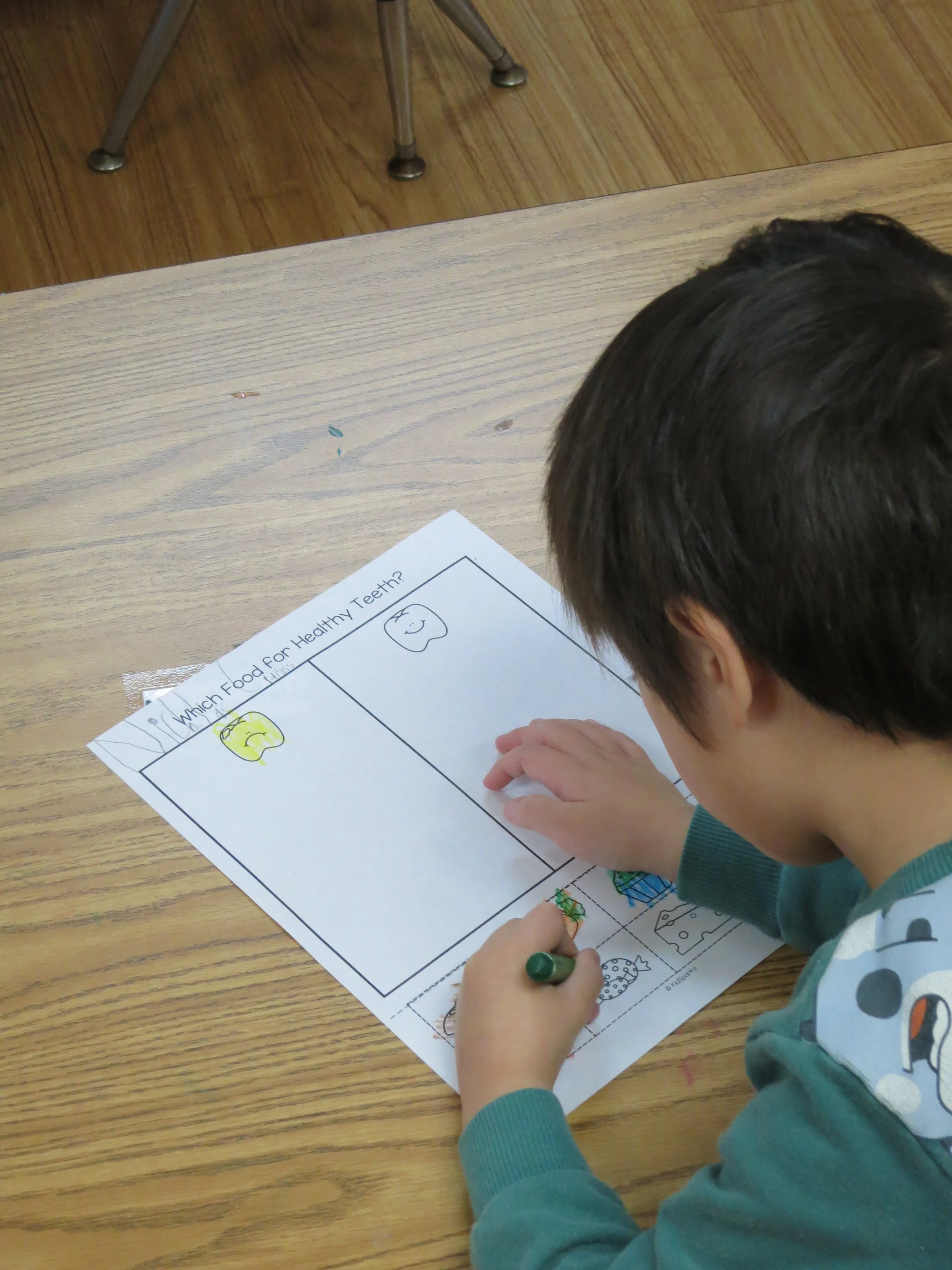 Preschool student coloring a worksheet with images of healthy and unhealthy teeth, titled "Which Food for Healthy Teeth?" (The Cross Schools of Education - Walnut, CA)