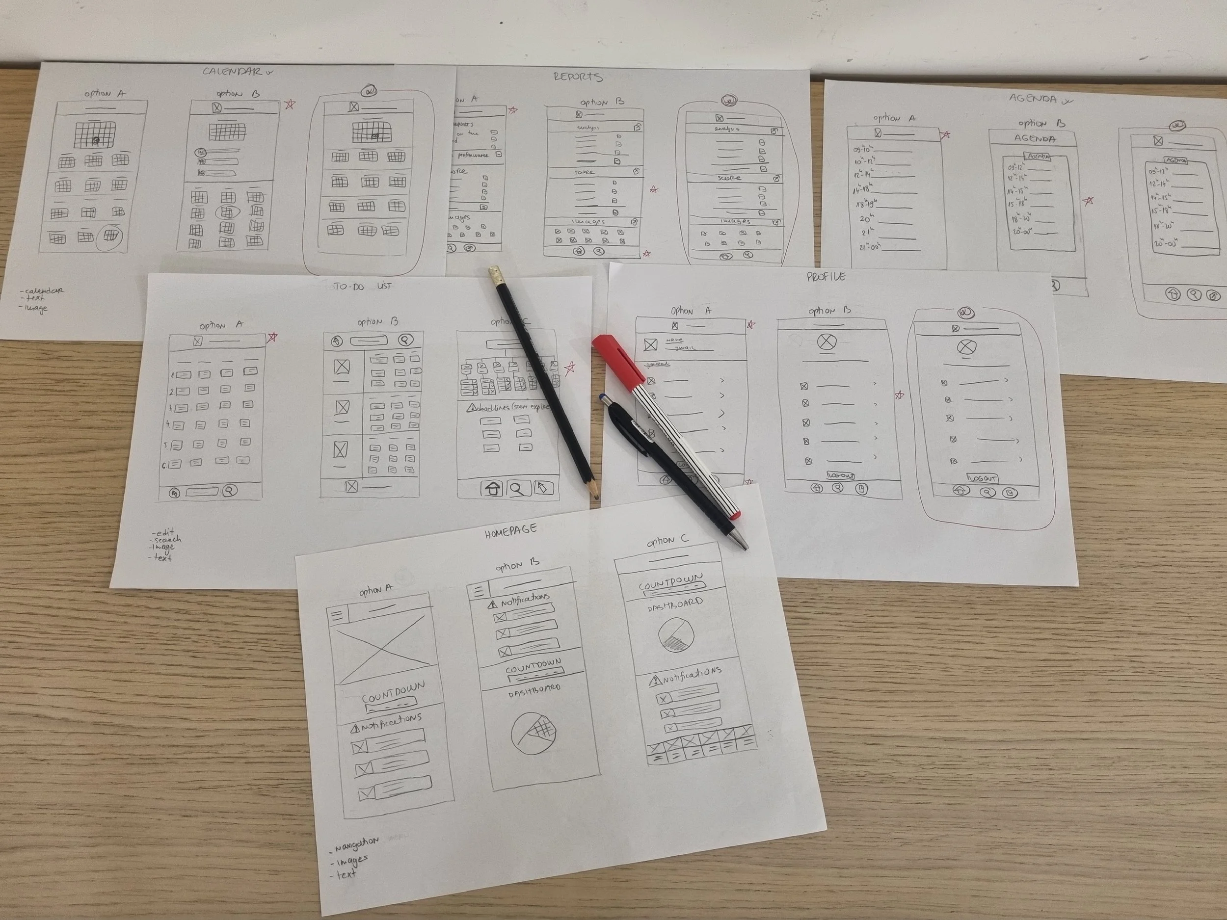 Sketches of mobile app interface designs and wireframes on several sheets of paper, with drawing pens placed on top of the papers.