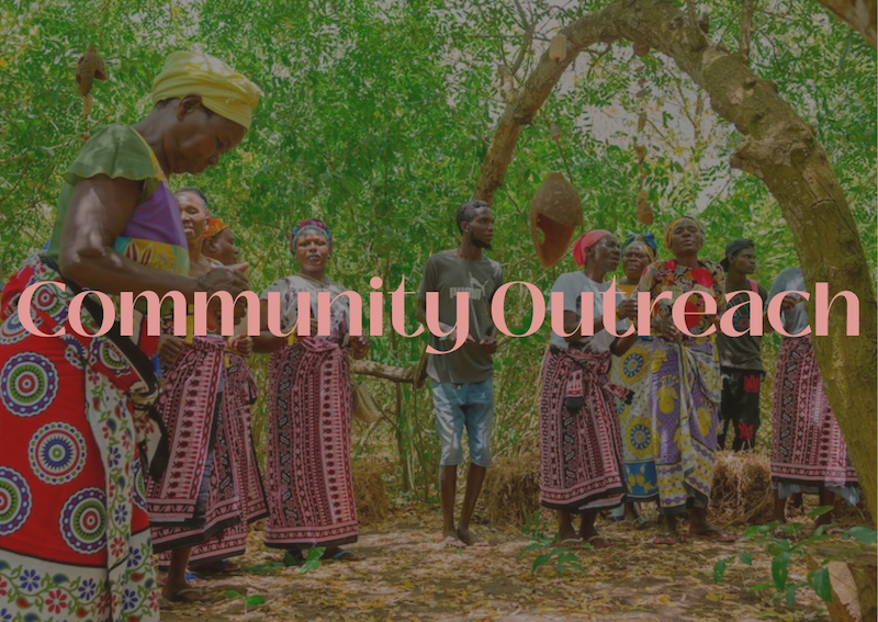 Group of people participating in community outreach, standing under a tree in an outdoor setting, with women dressed in colorful traditional clothing and a man in casual wear.