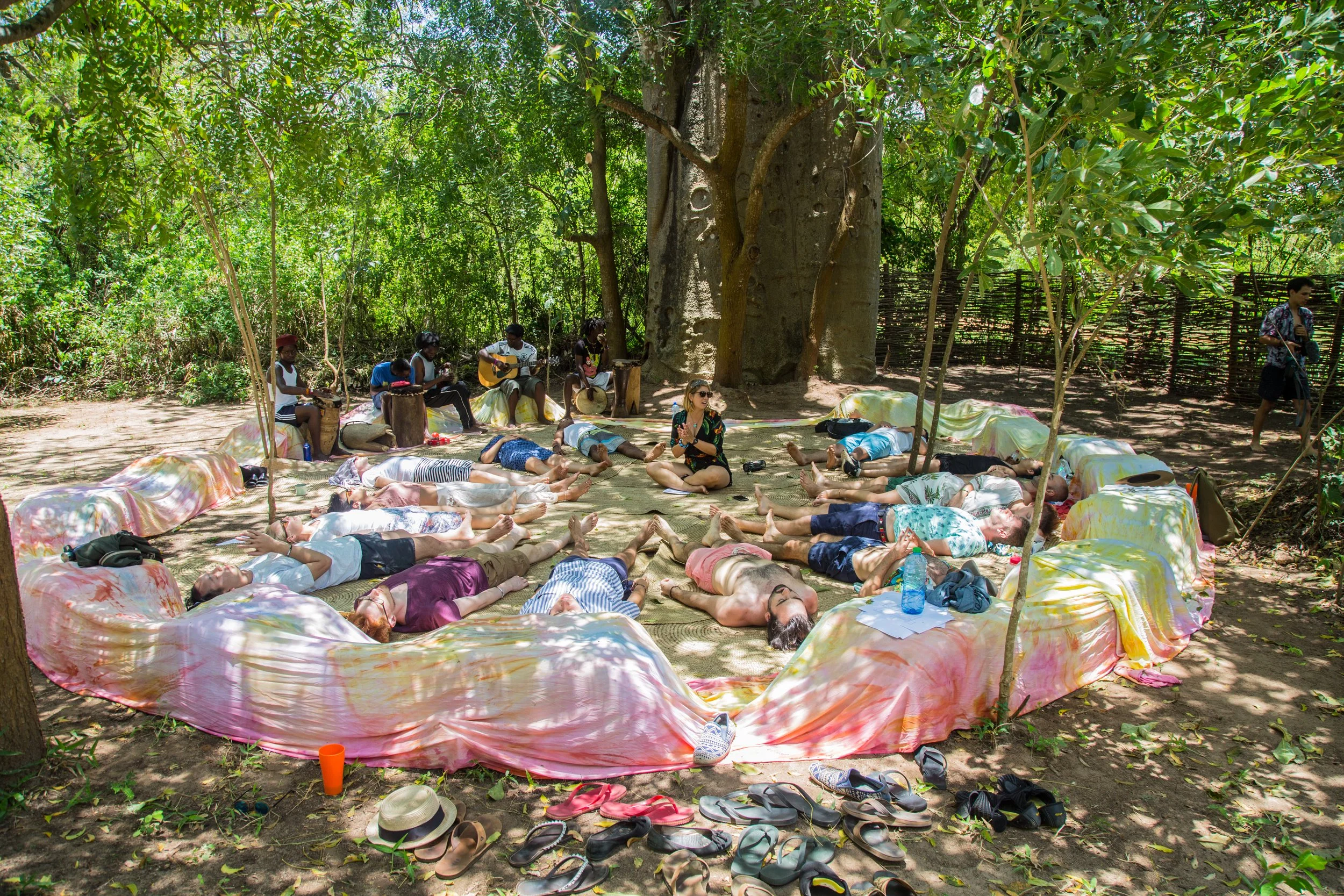 People practicing yoga outdoors under a tree in a wooded area. Outdoor wellness kilifi