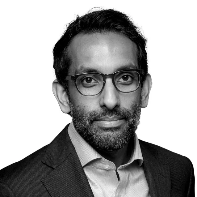 Black and white portrait of a man wearing glasses, a suit jacket, and a collared shirt