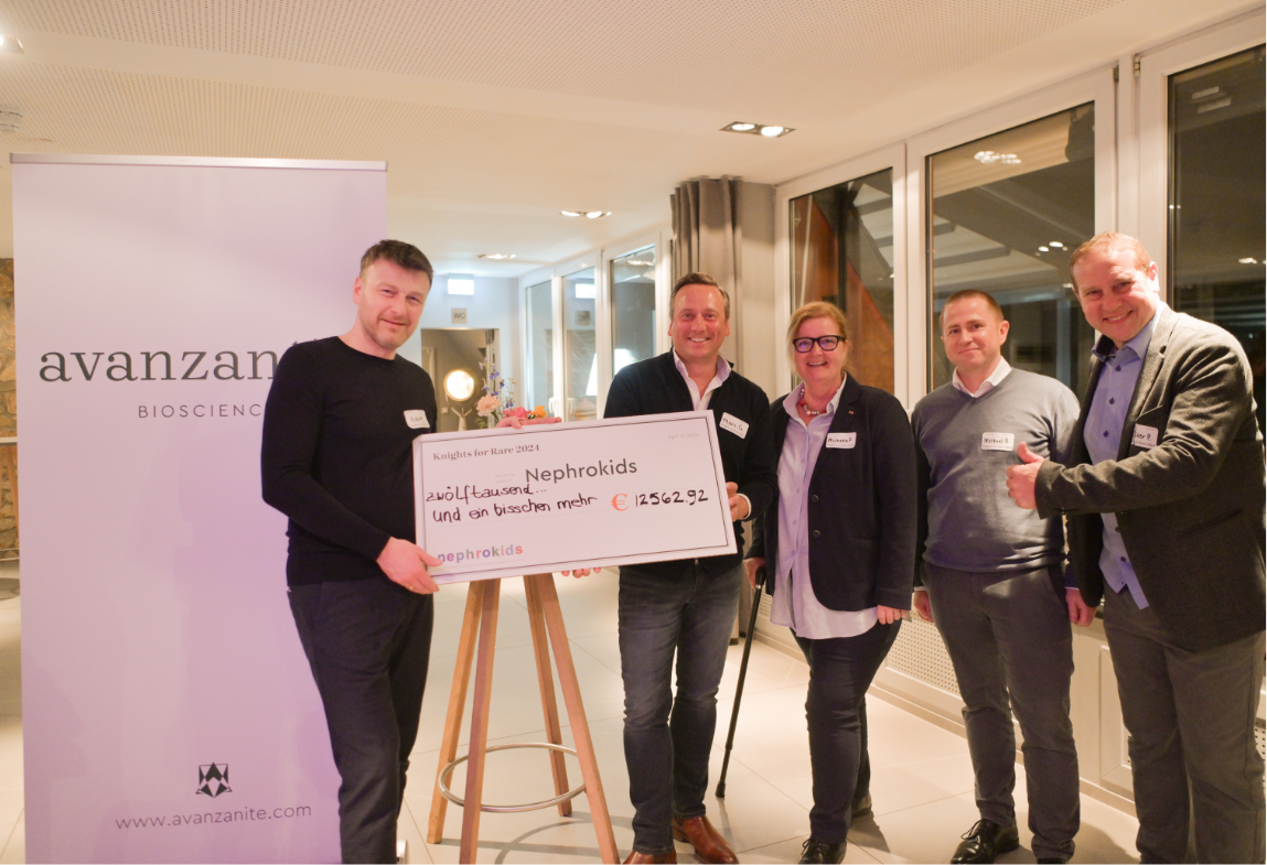 Group of five people holding a large check at an indoor event, with a banner in the background reading "avanzanite bioscience".