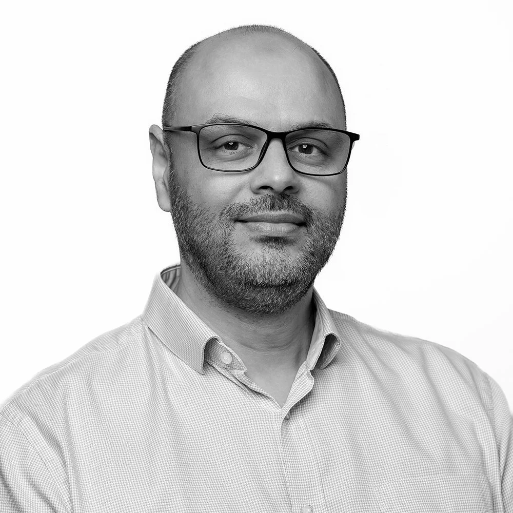 Black and white portrait of a middle-aged man with a beard, glasses, and wearing a collared shirt.