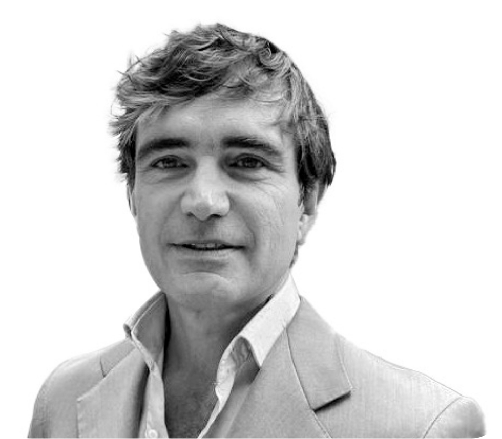 Black and white portrait of a man with wavy hair, wearing a collared shirt and blazer, smiling slightly against a plain white background.