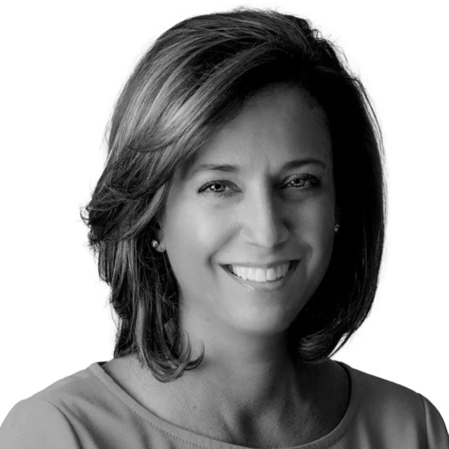Black and white headshot of a woman smiling, with shoulder-length hair, wearing a top with a rounded neckline and earrings.