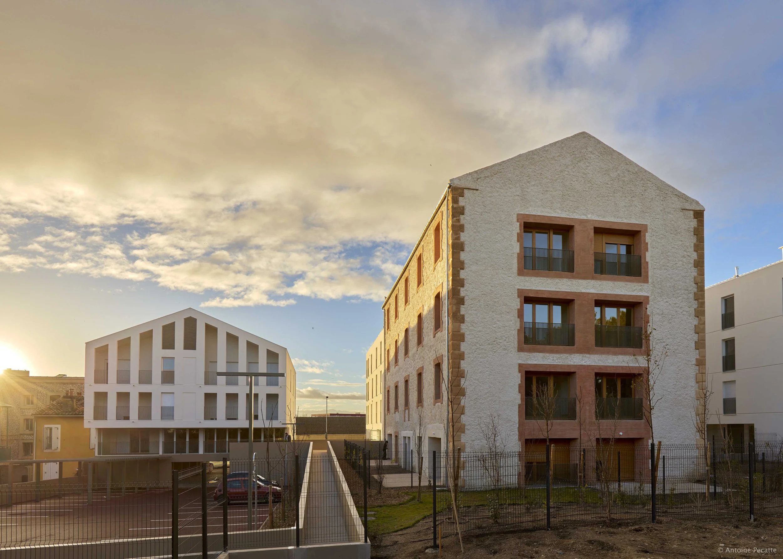 Bâtiments résidentiels modernes sous un ciel partiellement nuageux au coucher du soleil, avec un espace extérieur clôturé.