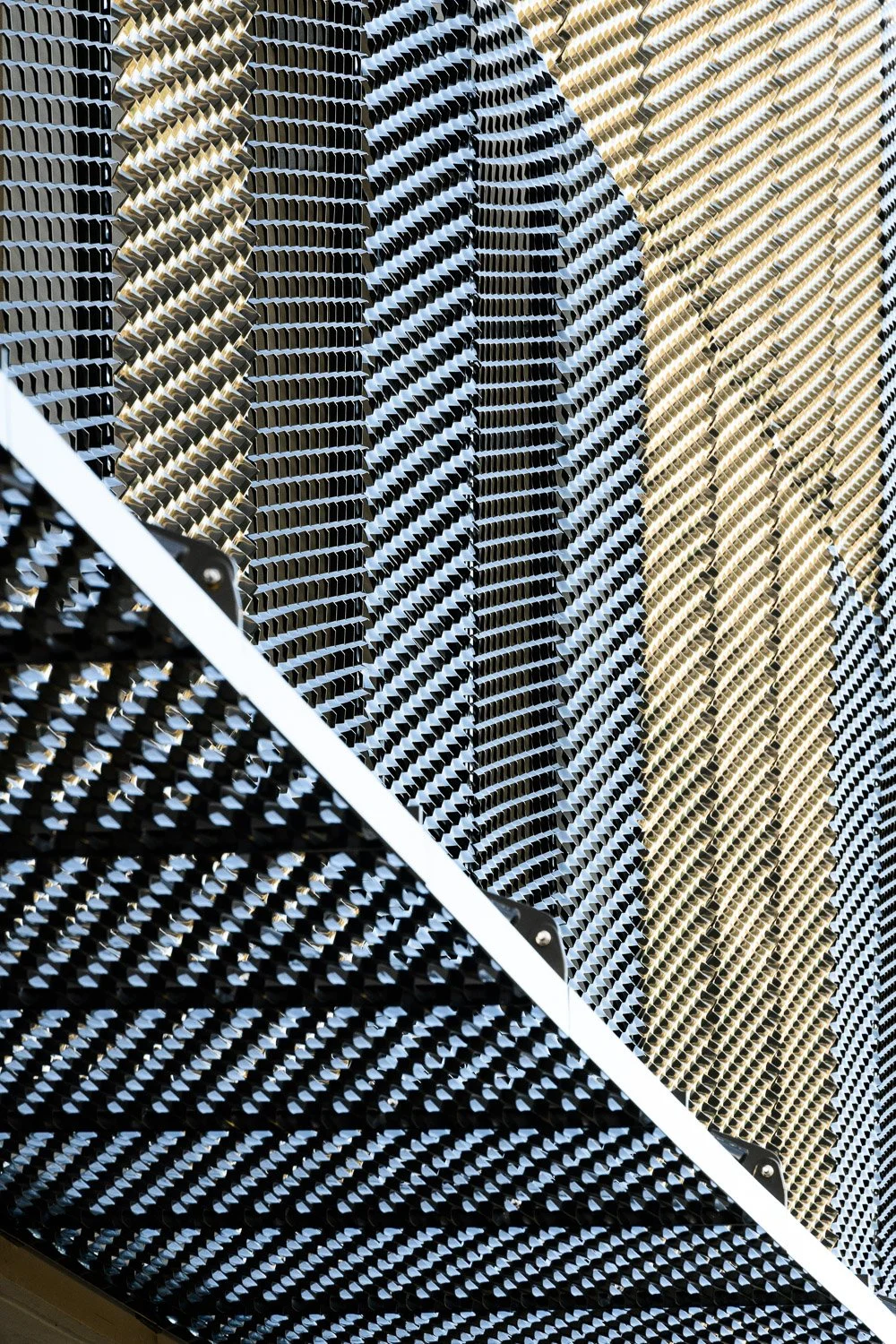 Vue en gros plan d'une façade en aluminium composée de motifs géométriques en forme de rectangles inclinés, la façade est divisée en sections de couleurs différentes : noir, argenté et doré.