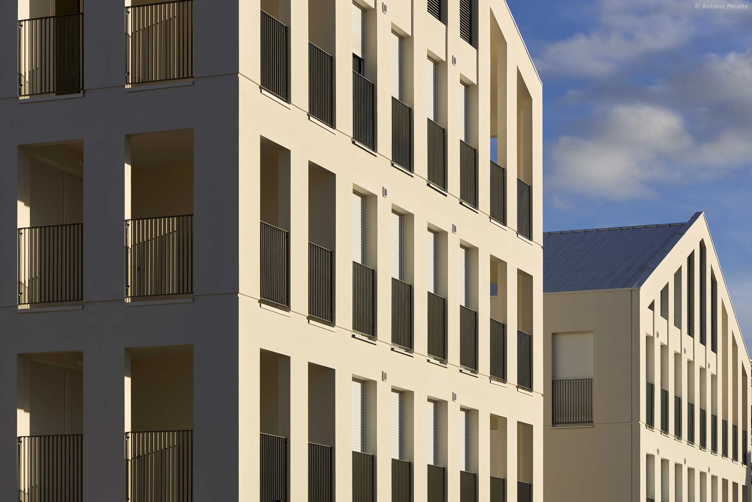 Deux bâtiments blancs modernes avec de nombreuses fenêtres et balcons, sous un ciel partiellement nuageux.