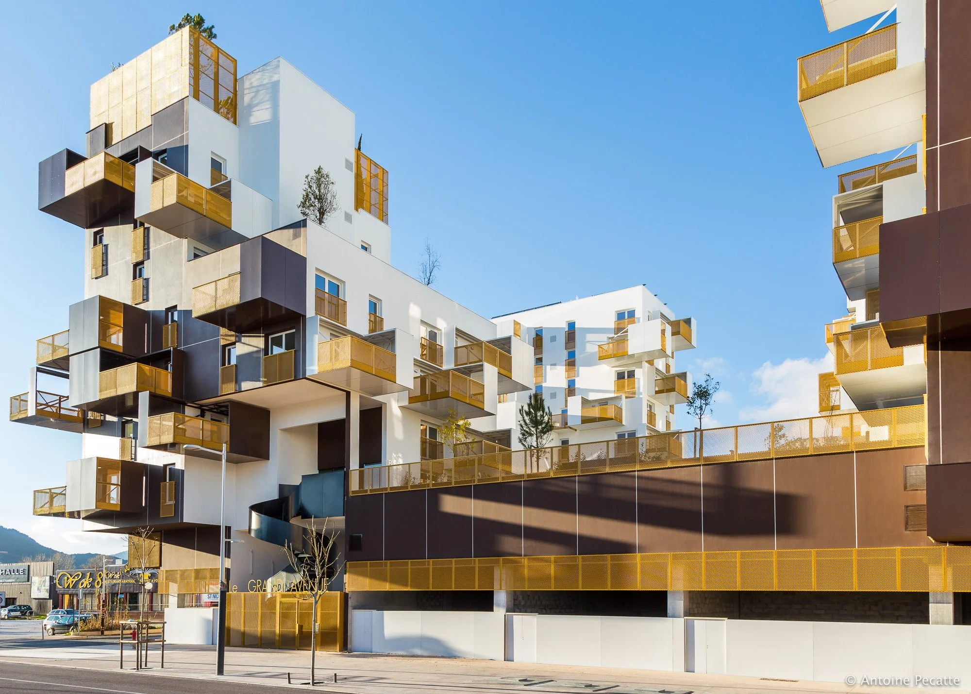 Un immeuble résidentiel moderne avec des balcons en verre doré et une architecture géométrique, sous un ciel bleu.