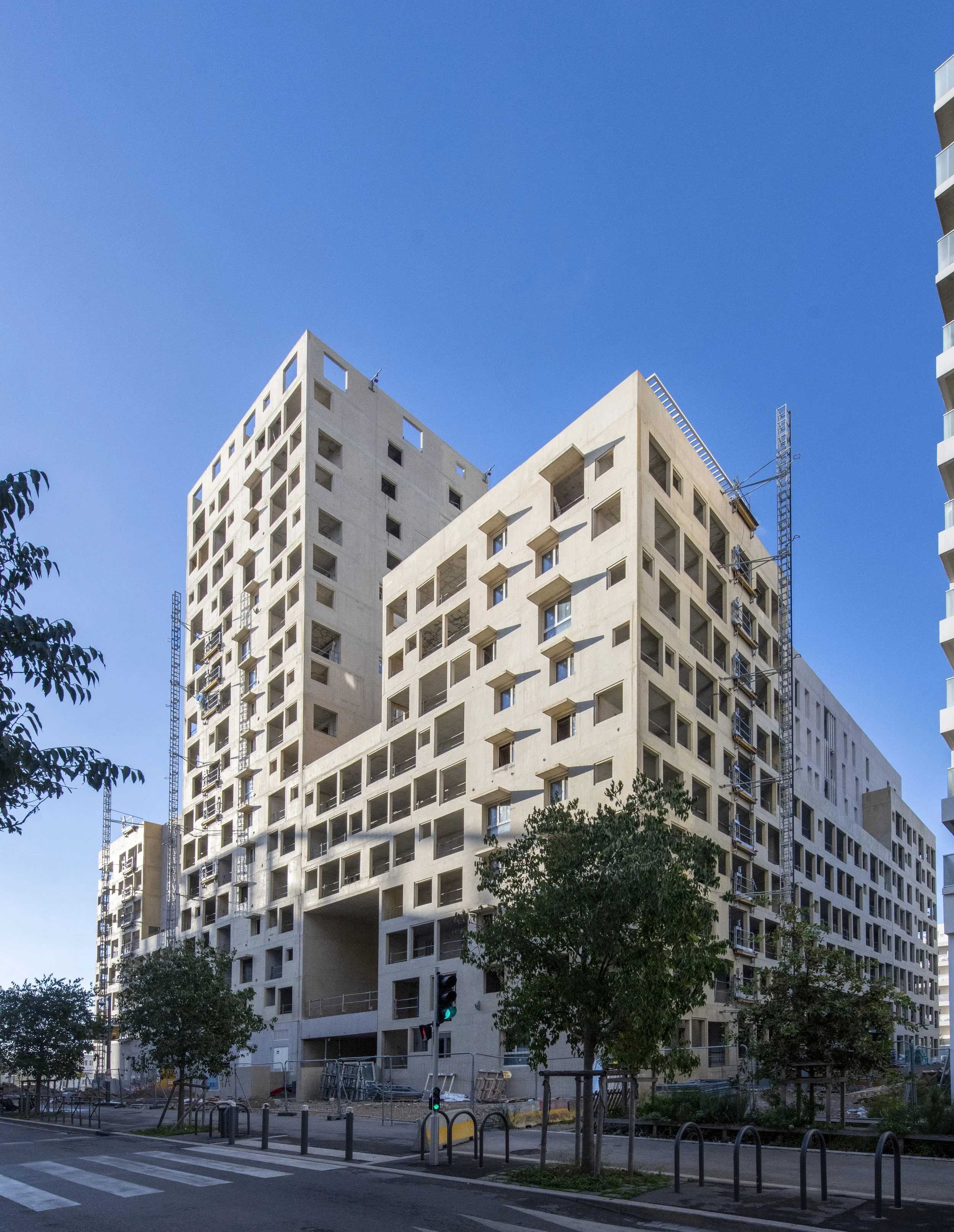 Construction d'un immeuble résidentiel moderne avec fenêtres carrées, sur un fond de ciel bleu.