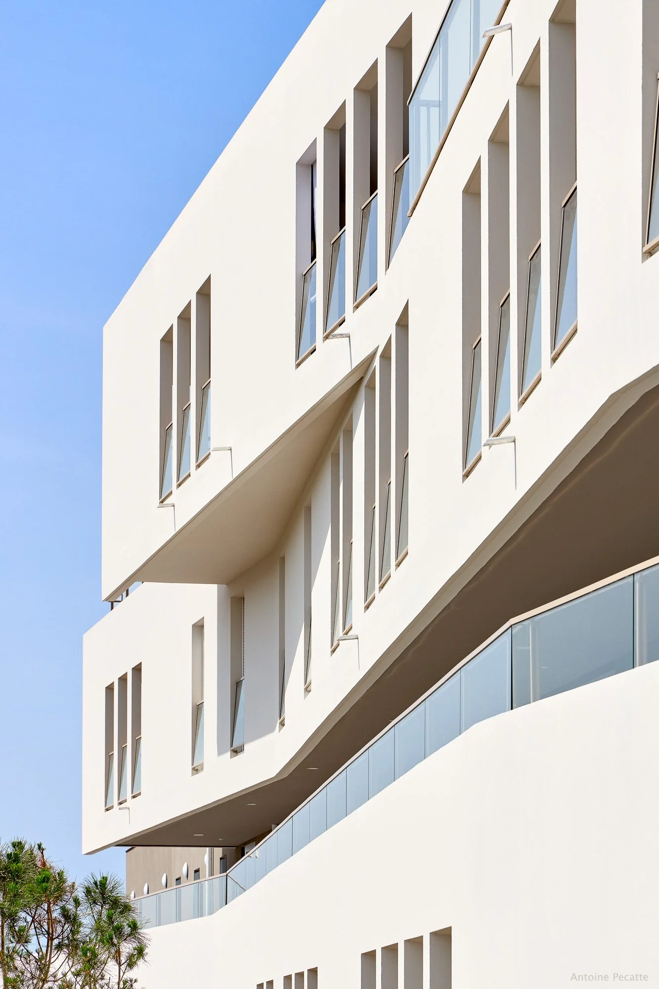Façade d'un bâtiment moderne blanc avec de nombreuses fenêtres, certains battants sont ouverts, sous un ciel bleu clair.