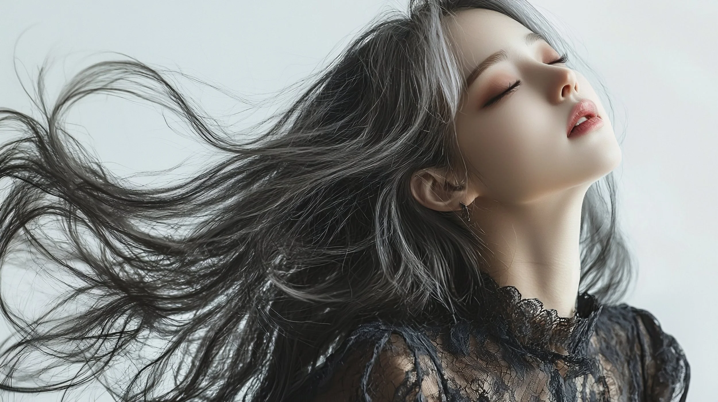 黒いレースのトップスを着た若い女性が、風に髪をなびかせながら目を閉じている