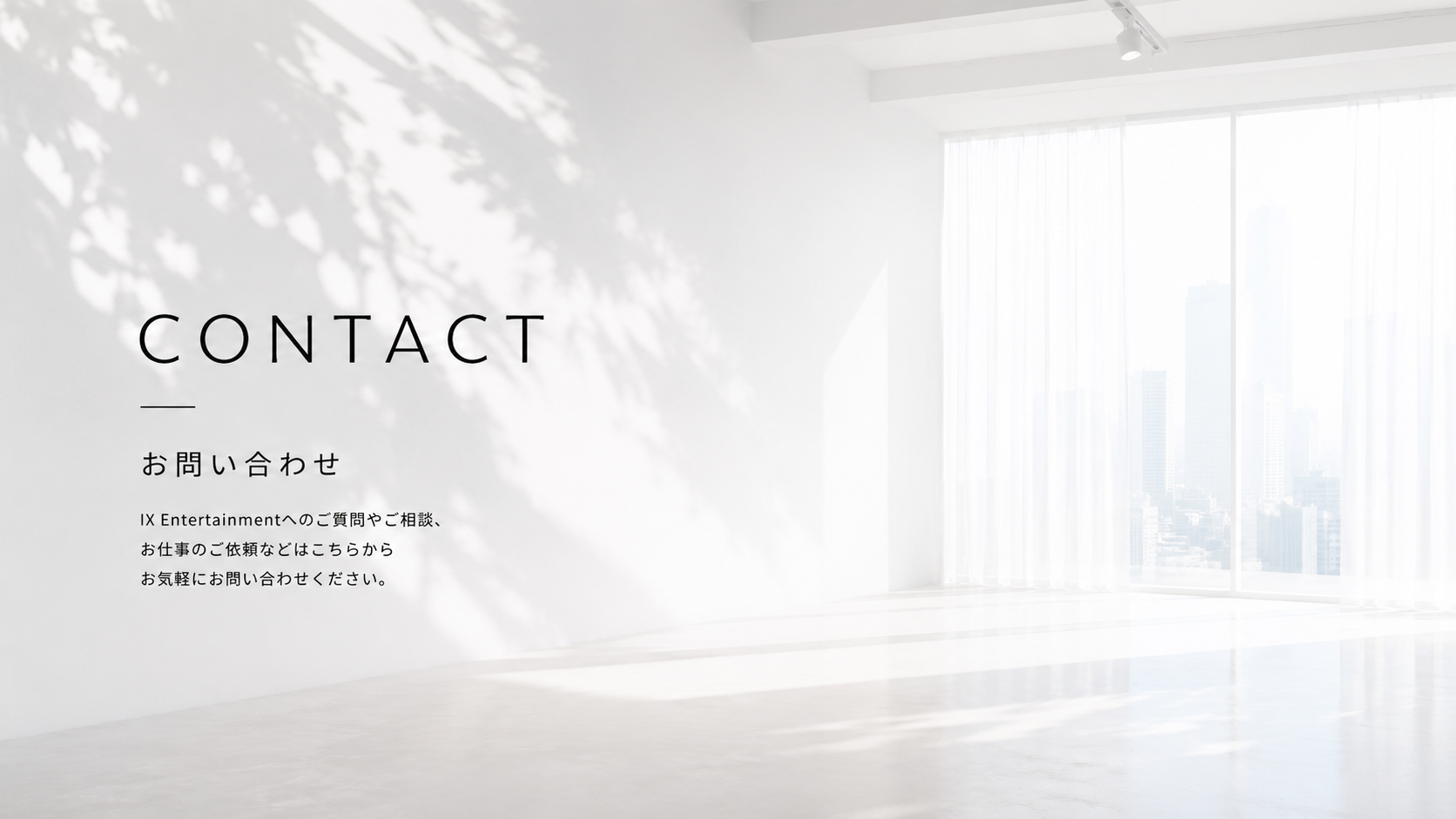 白い部屋の壁に黒い文字で「CONTACT」と書かれ、その下に日本語で問い合わせに関する説明がある。背景には大きな窓から都市のビル群が見える。」}**on the wall of a white room, saying