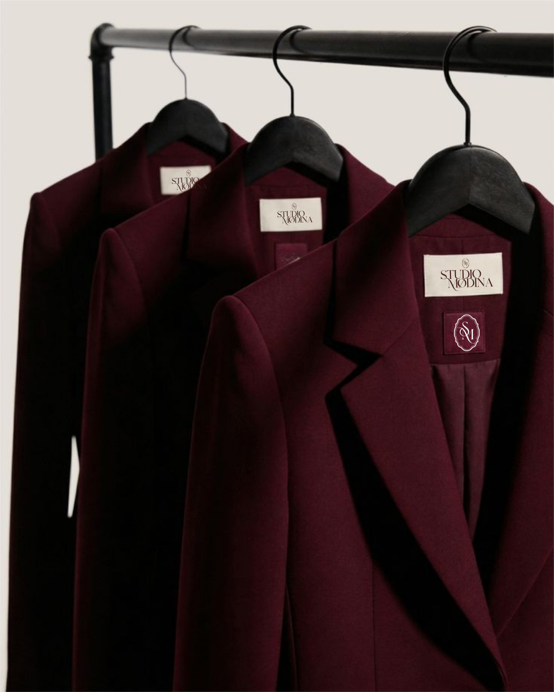 Three burgundy blazers hanging on black hangers on a black clothing rack.