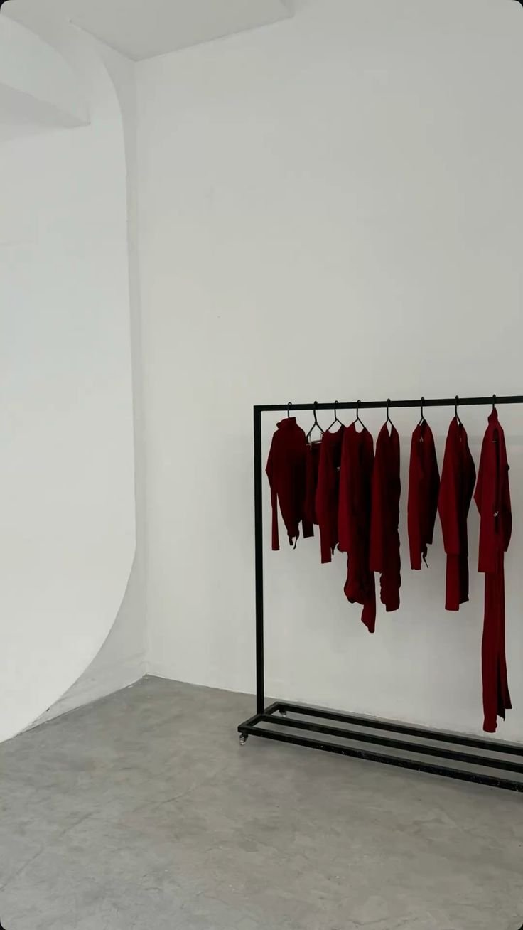 A black clothing rack with red clothing items hanging on it in a white room.