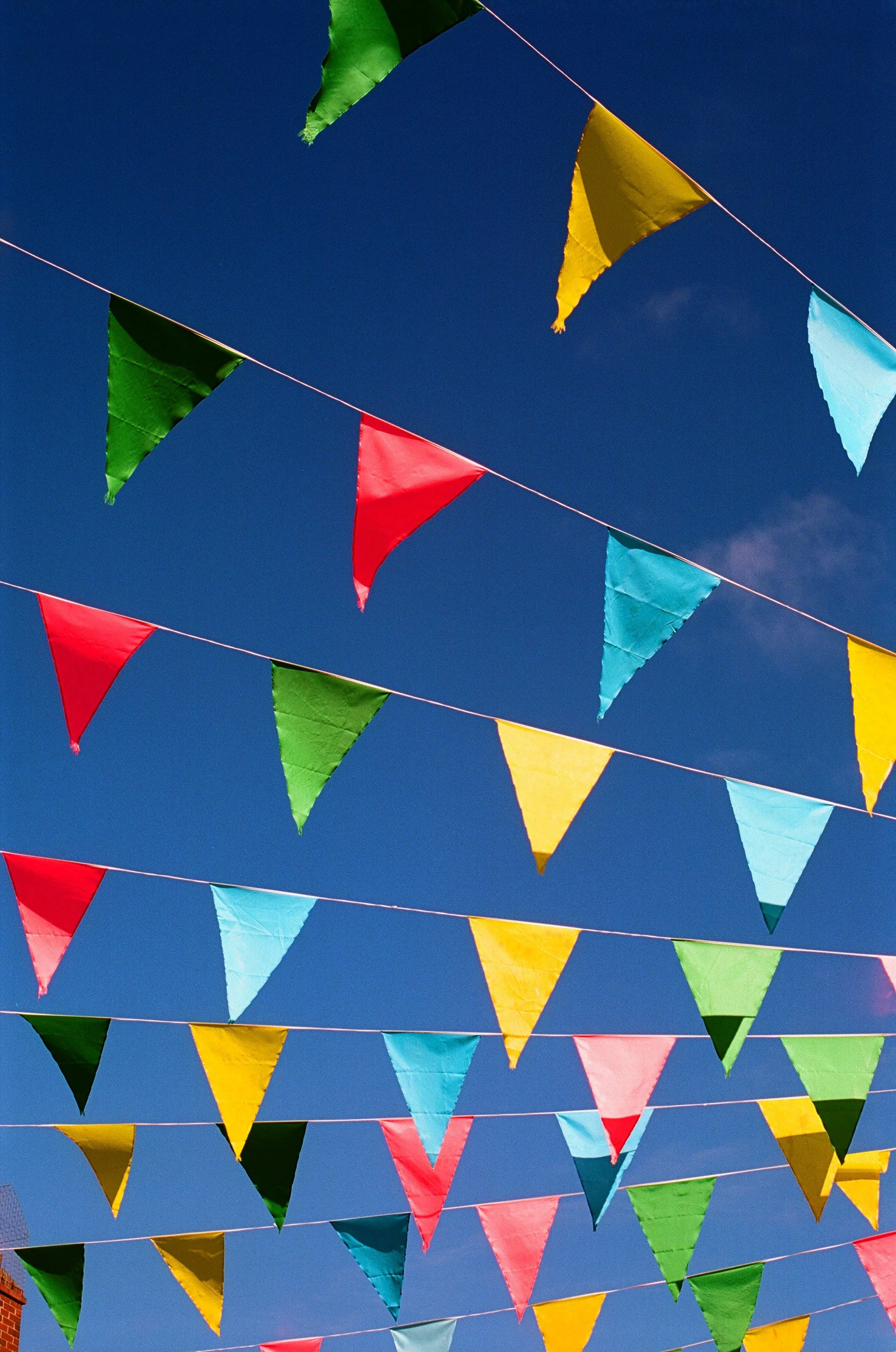 Colorful triangular pennant flags hanging against a clear blue sky.