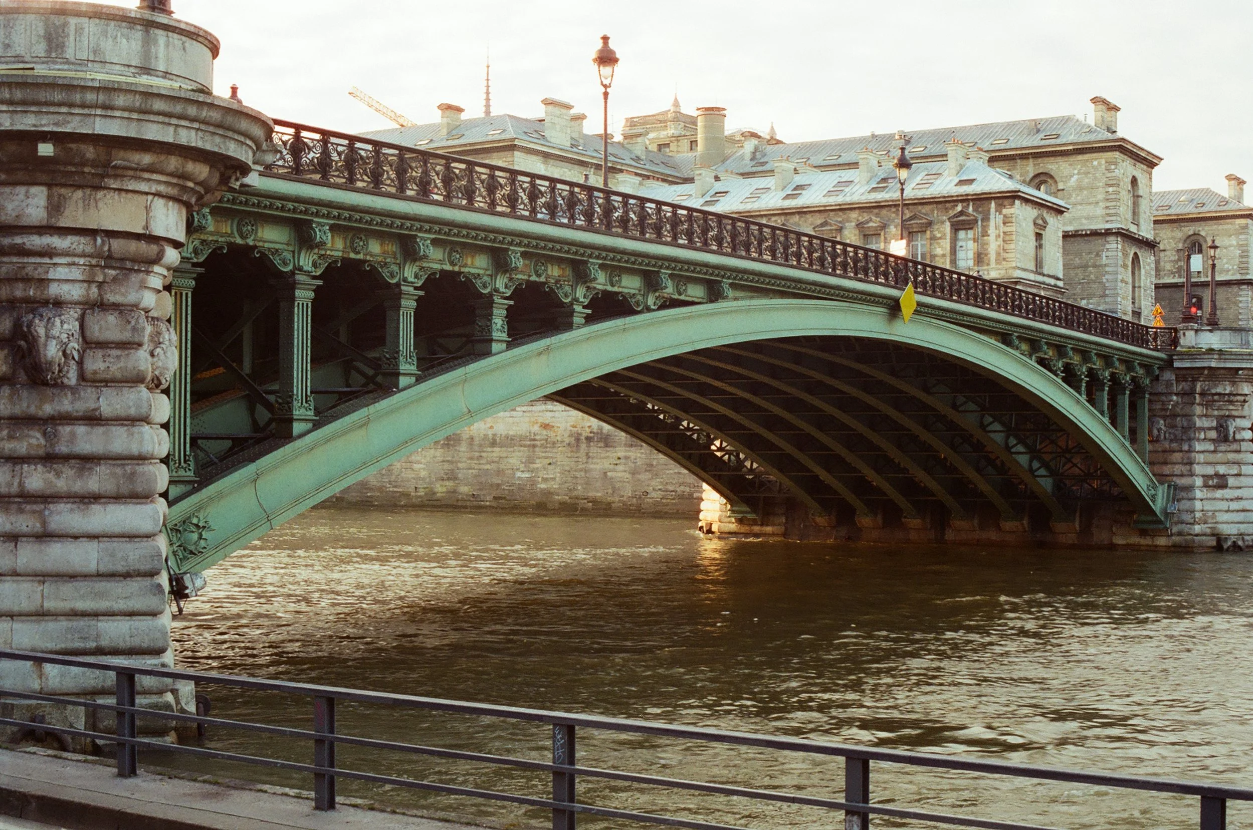 View of a historic bridge with ornate details crossing over a river, with classical buildings in the background.
