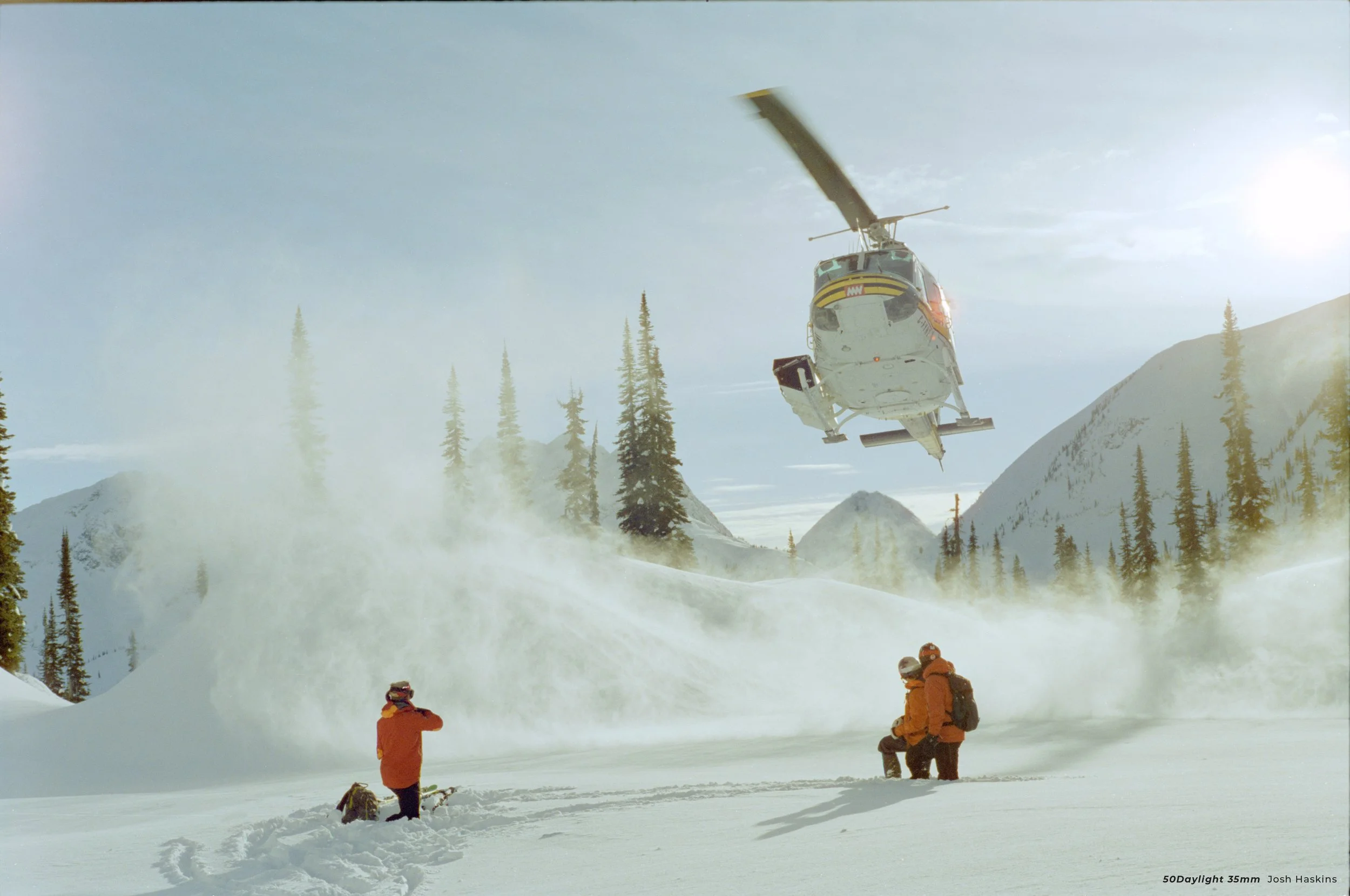 Cinestill 50D sample photo of a helicopter landing as two snowboarder watch on the side of a mountain
