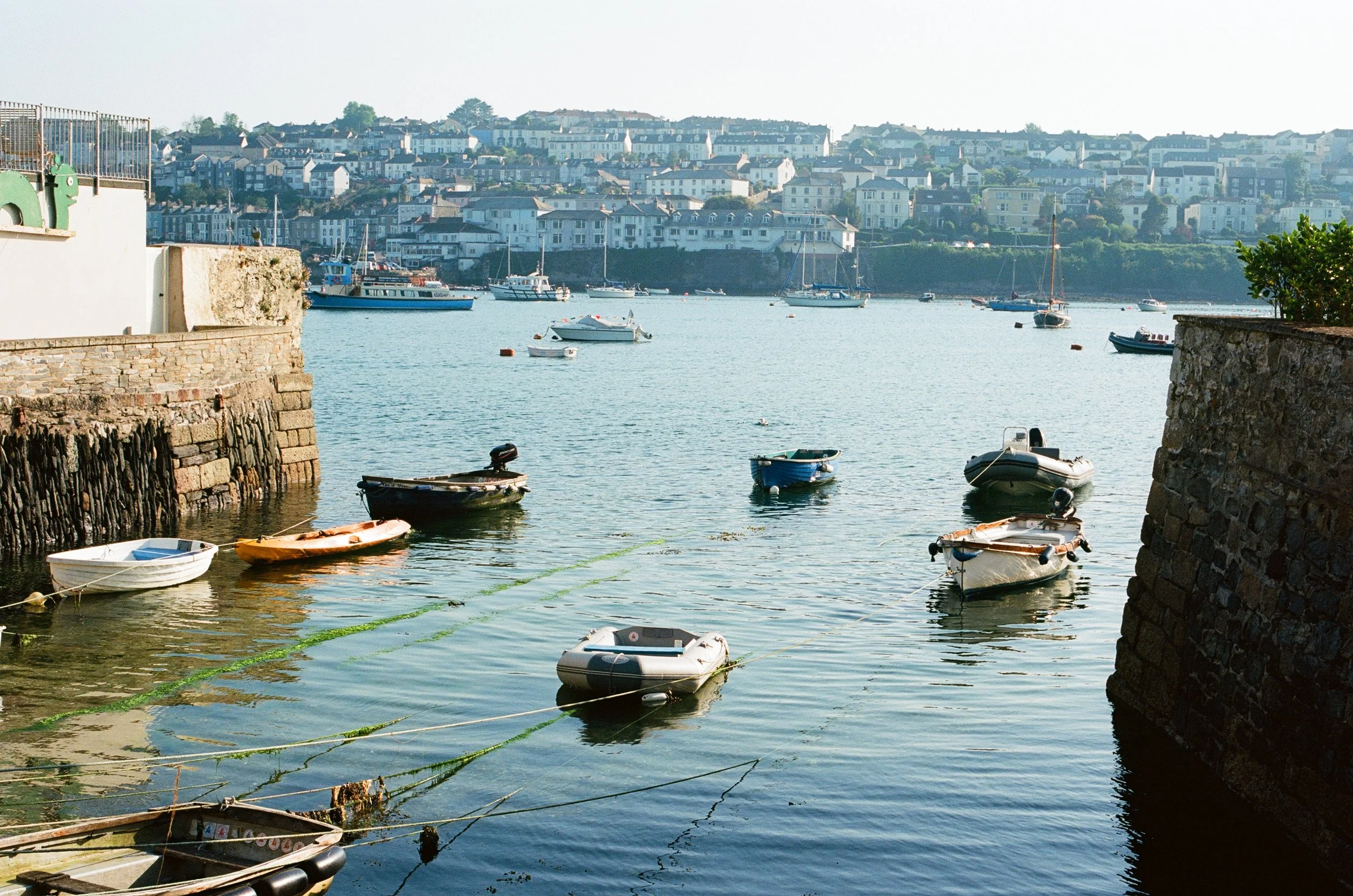 Boats docked at a harbor with a hillside town in the background.
