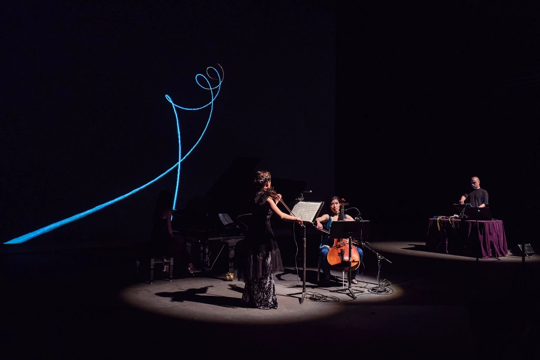 Musicians performing on stage with a large digital display of a stylized heart and smiley face drawn with blue neon lines in the background.