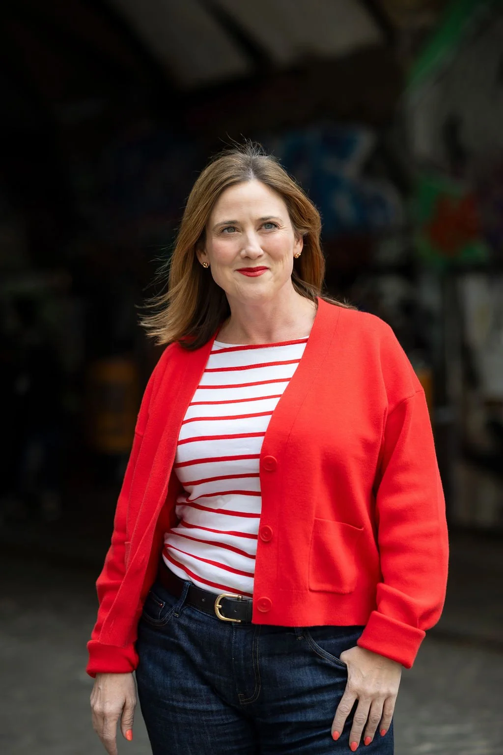 Sharon O'Dea, co-author of Digital Communications at Work, wearing a red cardigan over a white and red striped shirt, standing outdoors with her hand in her pocket.