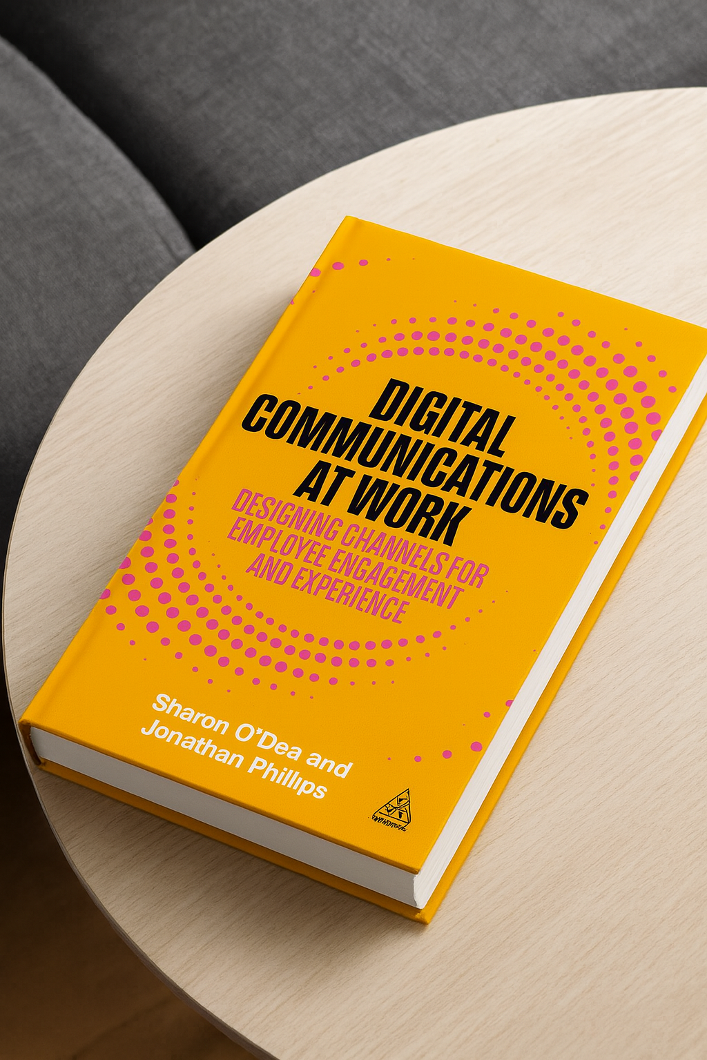 A yellow book titled 'Digital Communications at Work: Designing Channels for Employee Engagement and Experience' by Sharon O'Dea and Jonathan Phillips, resting on a light-colored round table, with a gray chair partially visible behind.