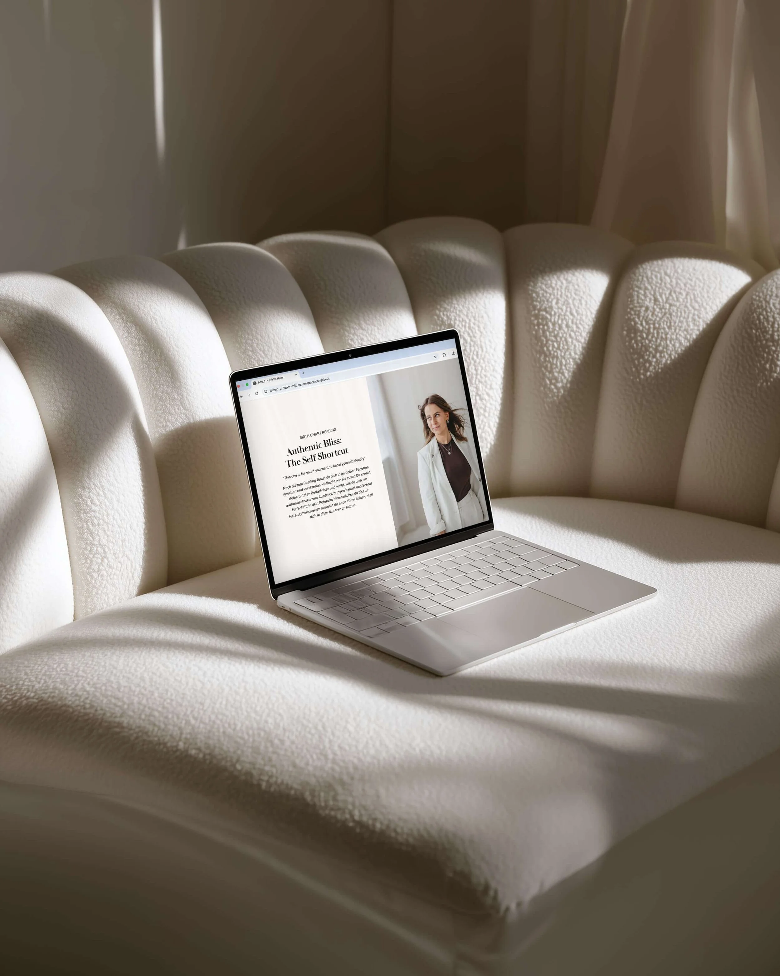 Ein  offener Laptop liegt auf einem cremefarbenen, gepolsterten Sofa, zeigt eine Webseite mit einem Bild Kristin in einem hellen Anzug.