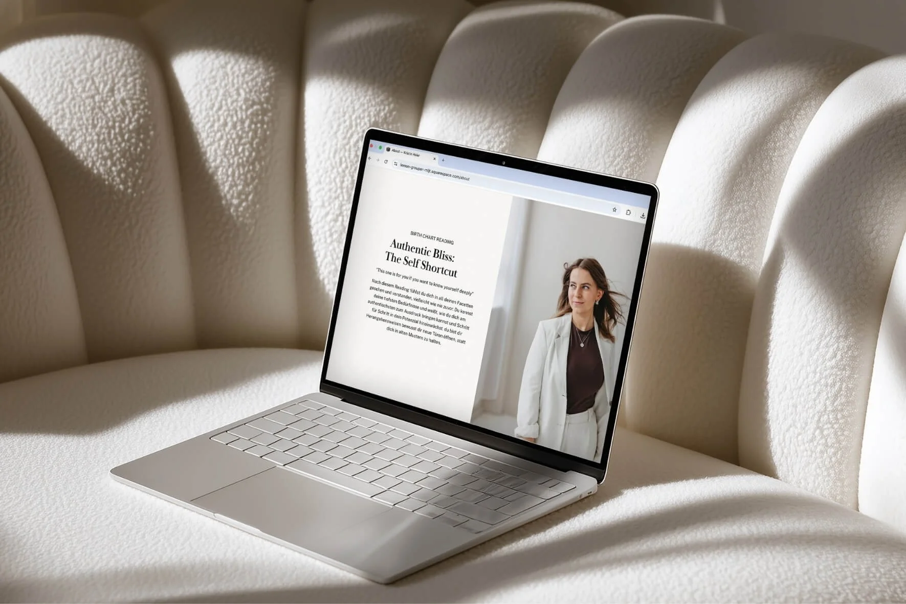 Ein  offener Laptop liegt auf einem cremefarbenen, gepolsterten Sofa, zeigt eine Webseite mit einem Bild Kristin in einem hellen Anzug.