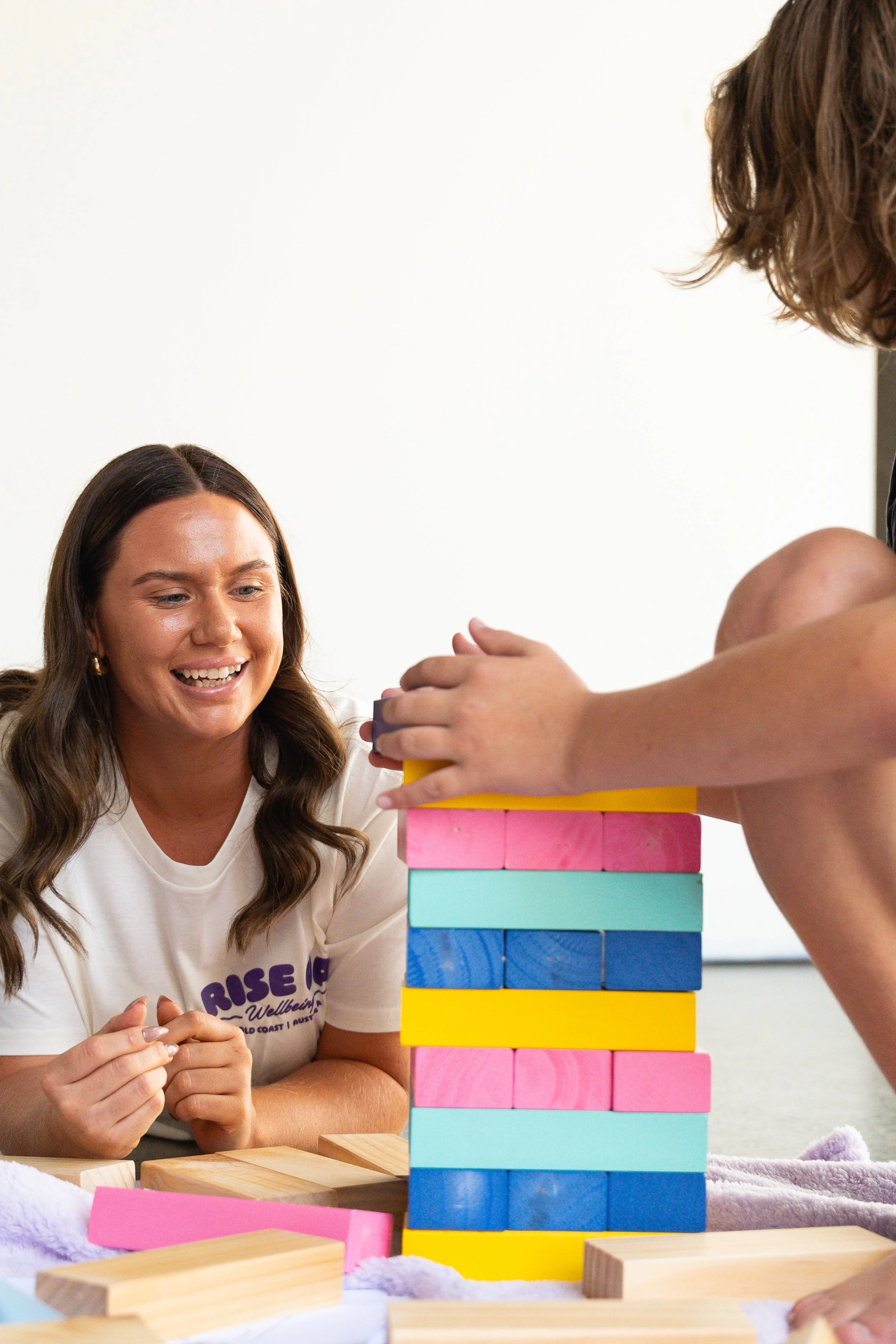 Two women playing Jenga with colorful wooden blocks at a table, smiling and focusing on the game.