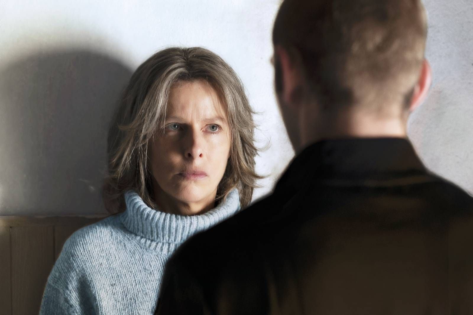Une femme à l'air sérieux regarde un homme dont le dos est visible, dans une lumière tamisée.