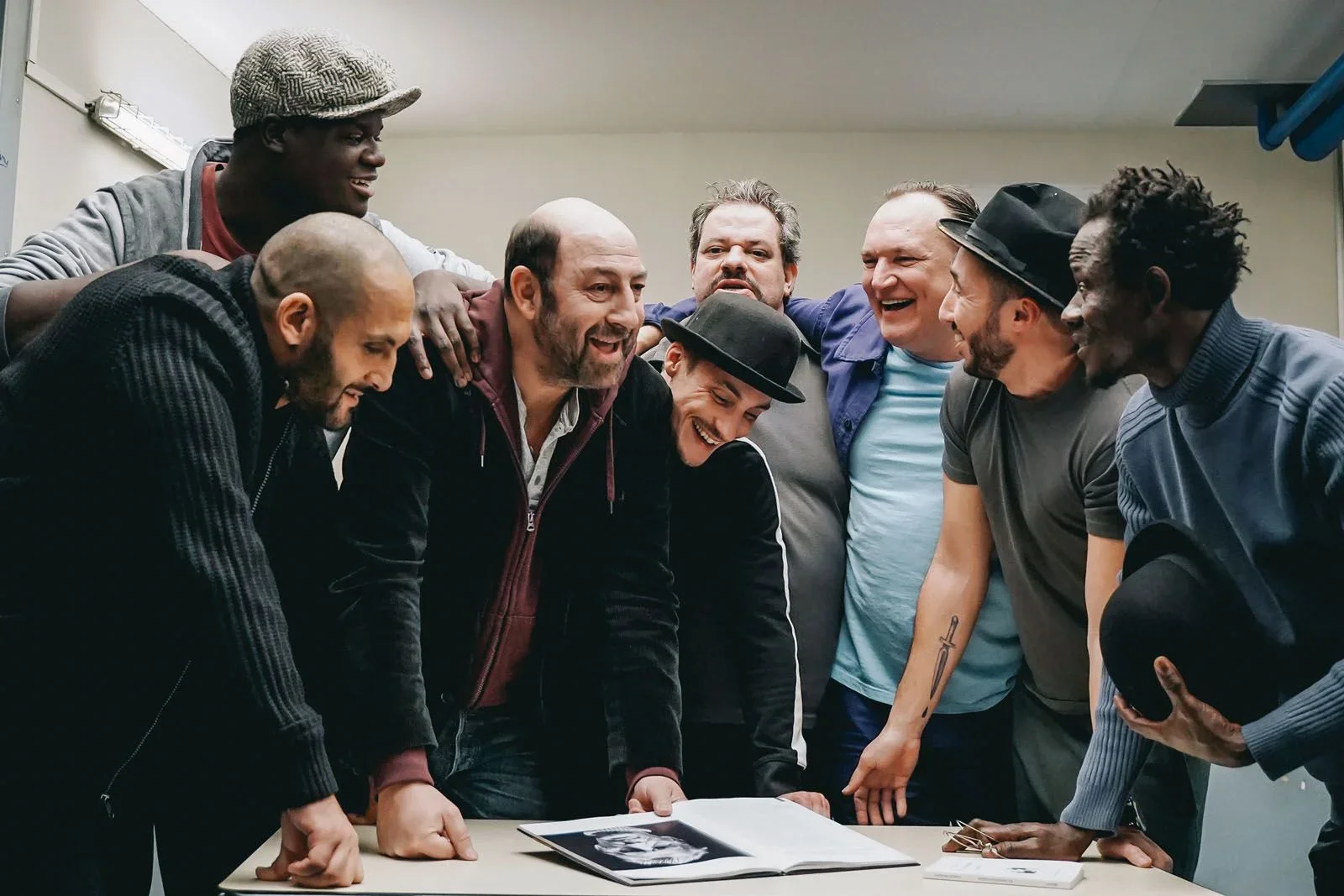 Groupe de personnes joyeuses autour d'une table regardant un album photo ou radiographie, dans une salle d'accueil. Ils sourient et rient ensemble.