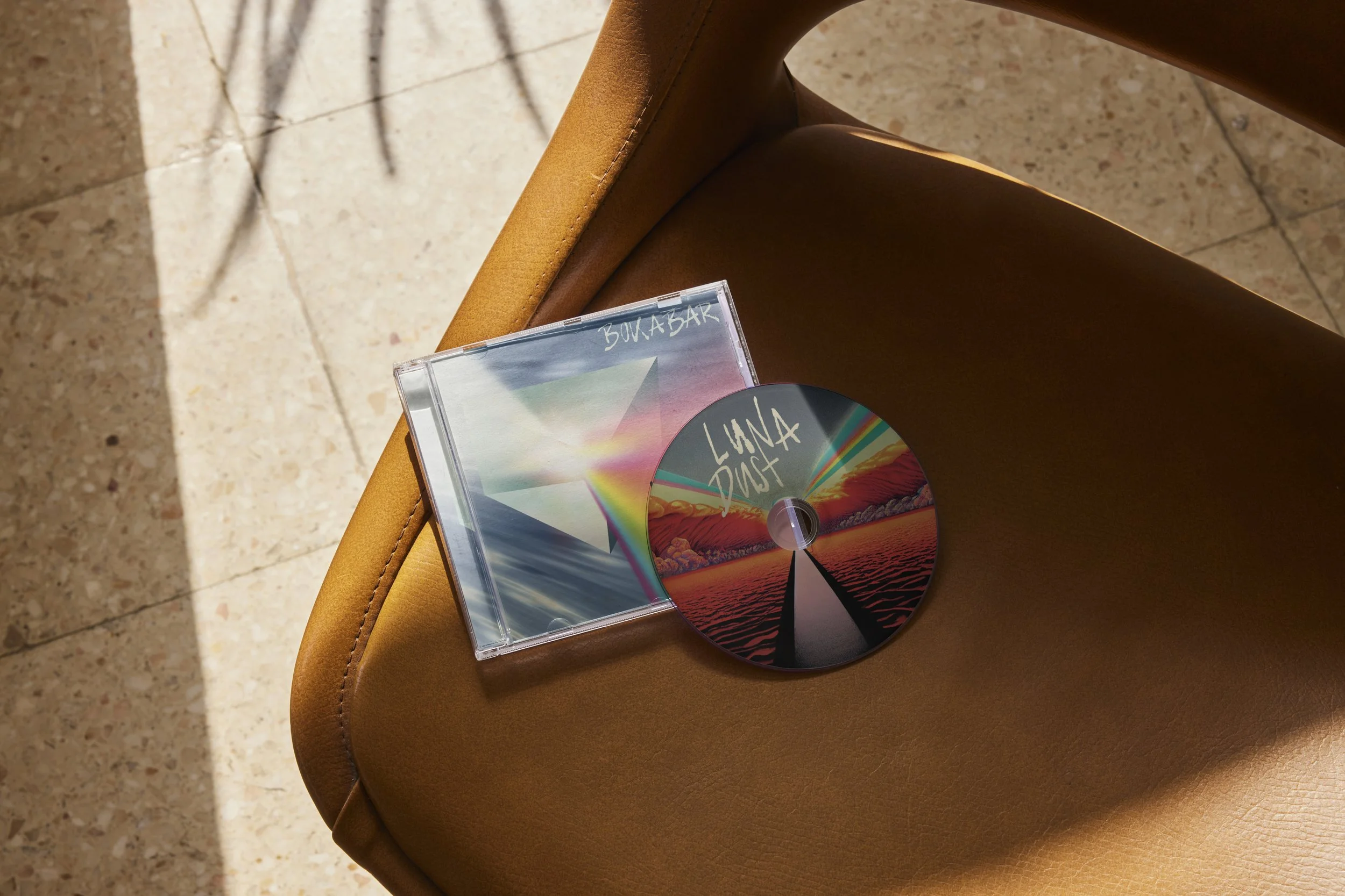 Une pochette d'album avec un disque et un boîtier en plastique repose sur une chaise en cuir de couleur marron clair, avec un sol en pierre au fond.