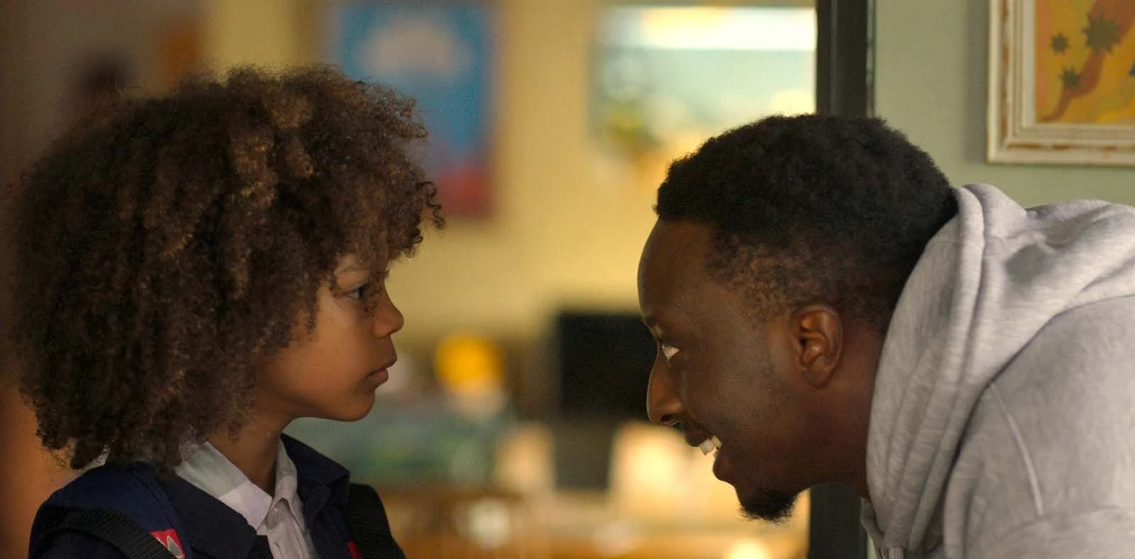 Un adulte et un enfant se regardent intensément, se trouvant très proches, dans une pièce intérieure.