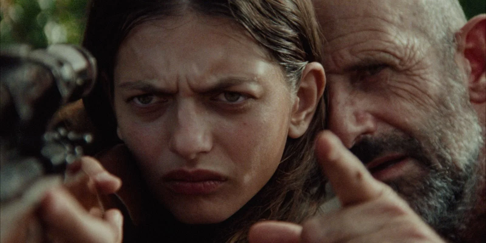 Un jeune femme et un vieil homme regardant à travers un viseur d'arme, avec expressions concentrées et intensives.