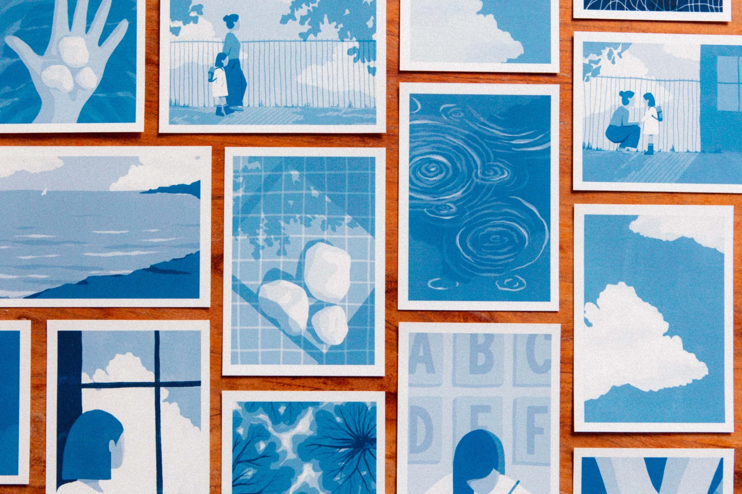 Collection d'illustrations en nuances de bleu représentant des paysages, des objets et des scènes de la vie quotidienne, affichées sur une surface en bois.