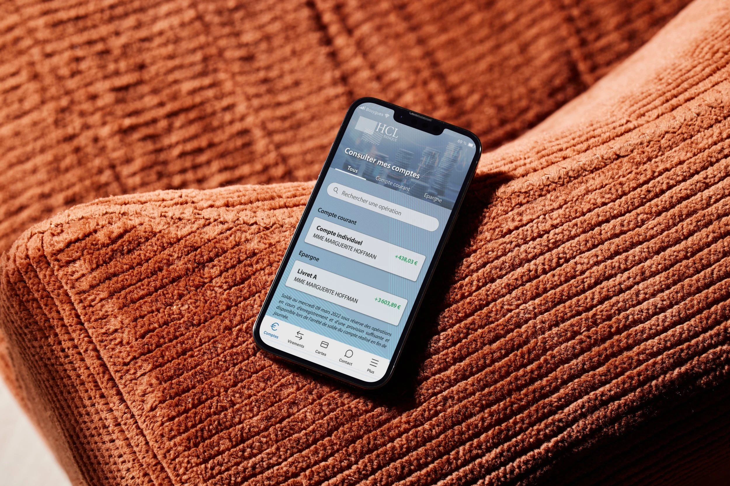 Téléphone affichant une application bancaire reposant sur un canapé orange en tissu côtelé.