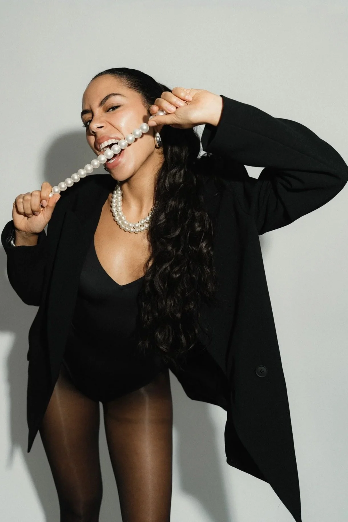 Frau mit schwarzen Haaren in schwarzer Kleidung, die eine Perlenkette hält und bei einem lustigen Fotoshooting spielt.