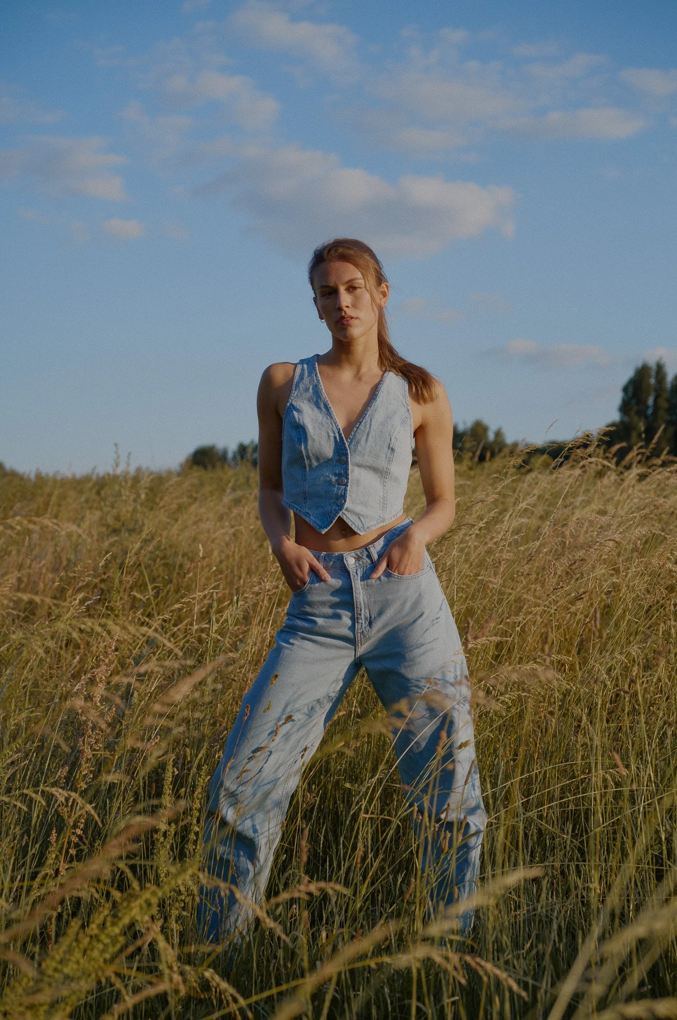 Junge Frau in Jeansoutfit im Feld bei Sonnenuntergang.