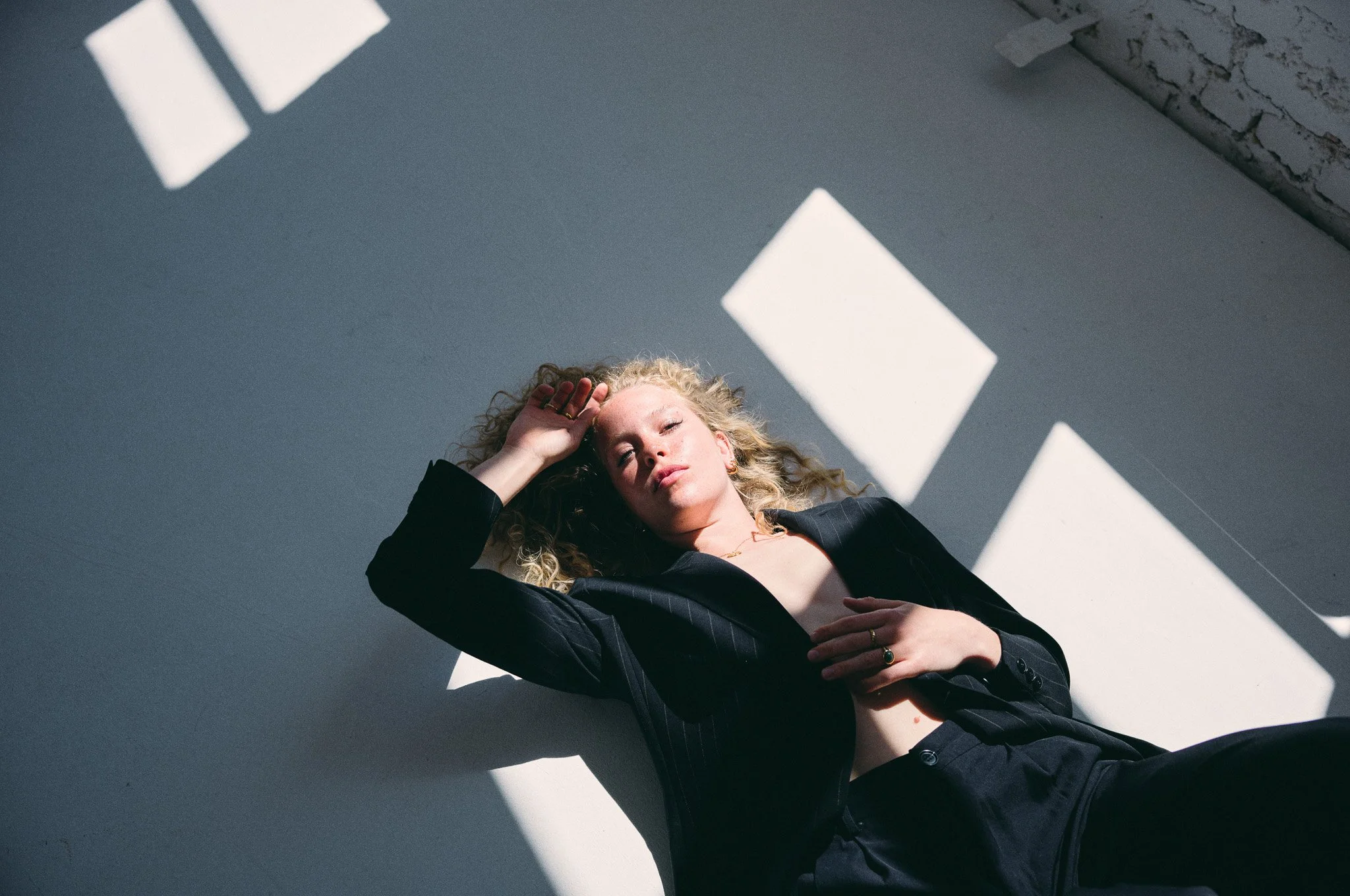 Frau liegt auf dem Boden, Sonnenlicht strömt durch Fenster und erzeugt Schatten auf ihrem Gesicht und der Wand.