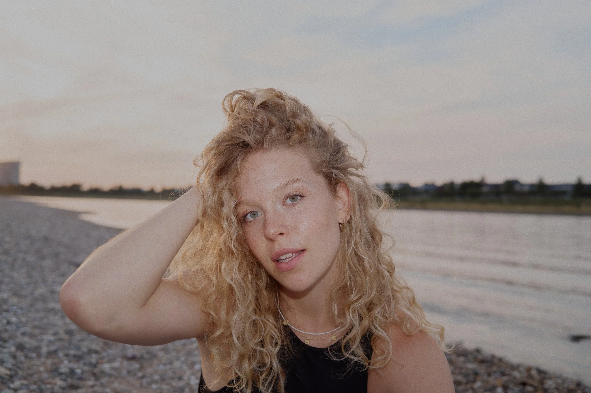 Junge Frau mit lockigem blonden Haar am Strand bei Sonnenuntergang