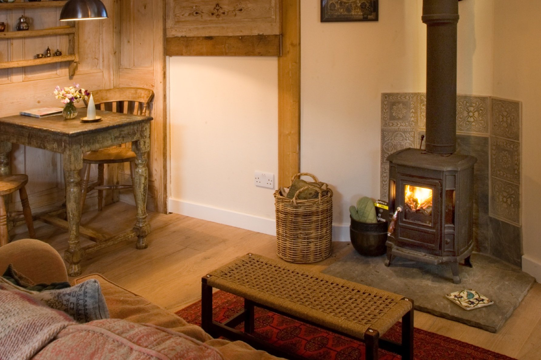 Cozy living room corner with pellet stove burning, woven baskets, wooden furniture, and decorative accents.