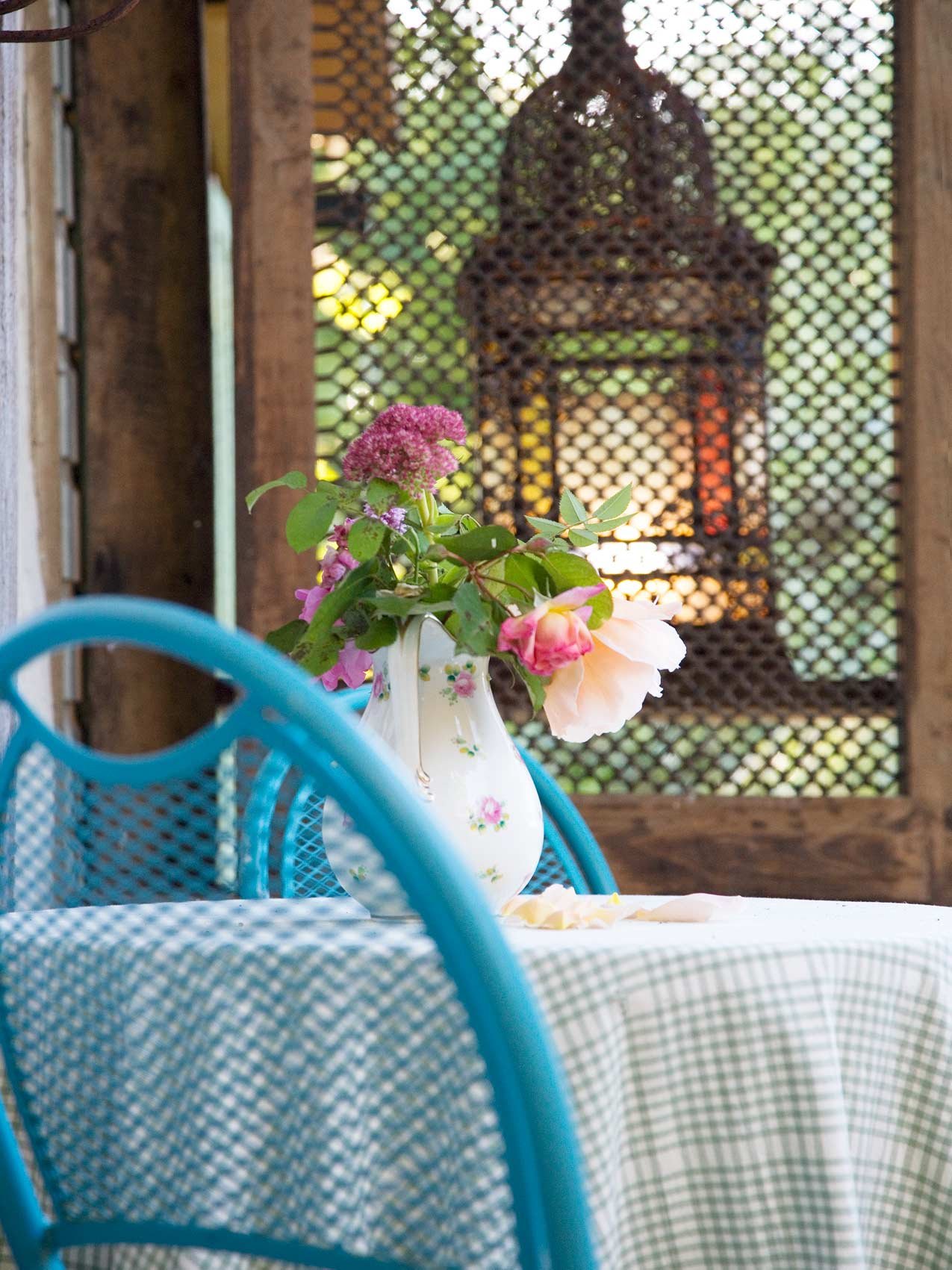 A tabletop with a floral vase, blue chairs, and a lantern hanging on a lattice background.