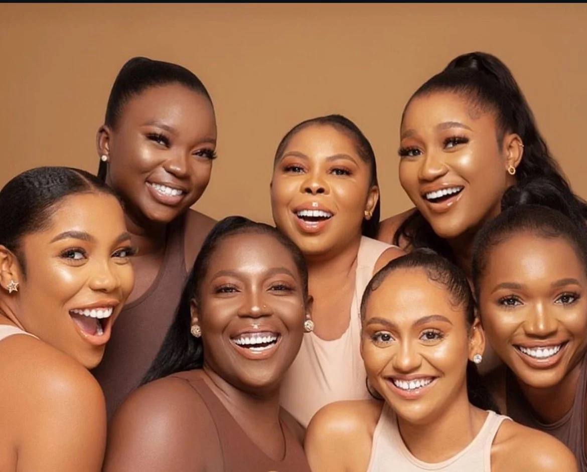 Seven women smiling happily in a group photo, with a warm beige background.