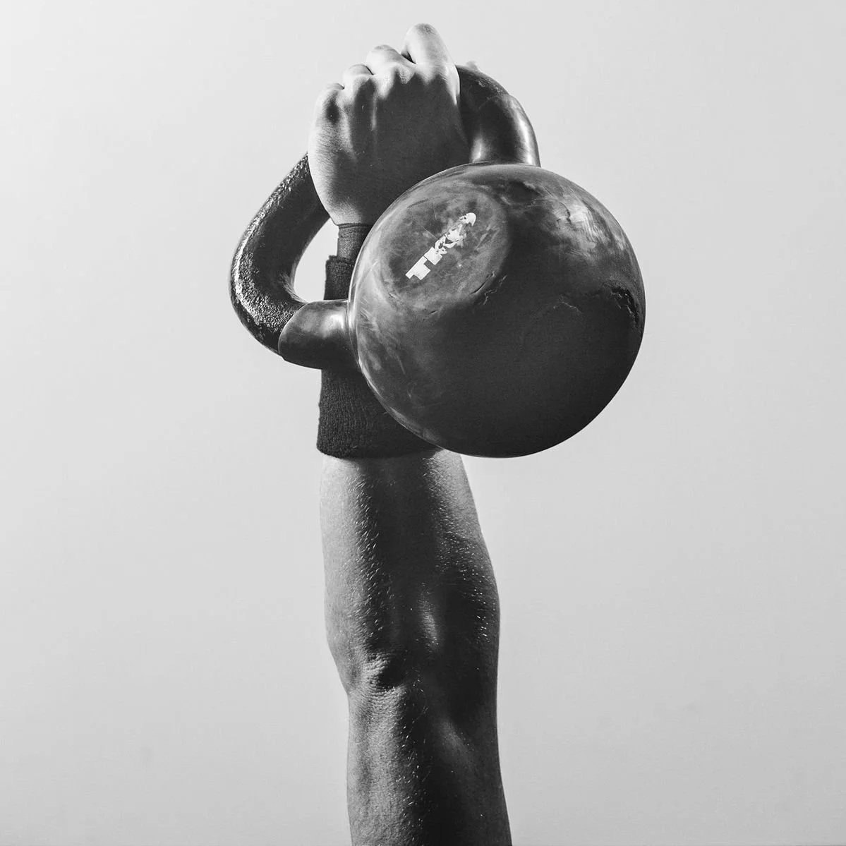A black and white photo of a person's arm holding a kettlebell with the letters 'TRX' on it.