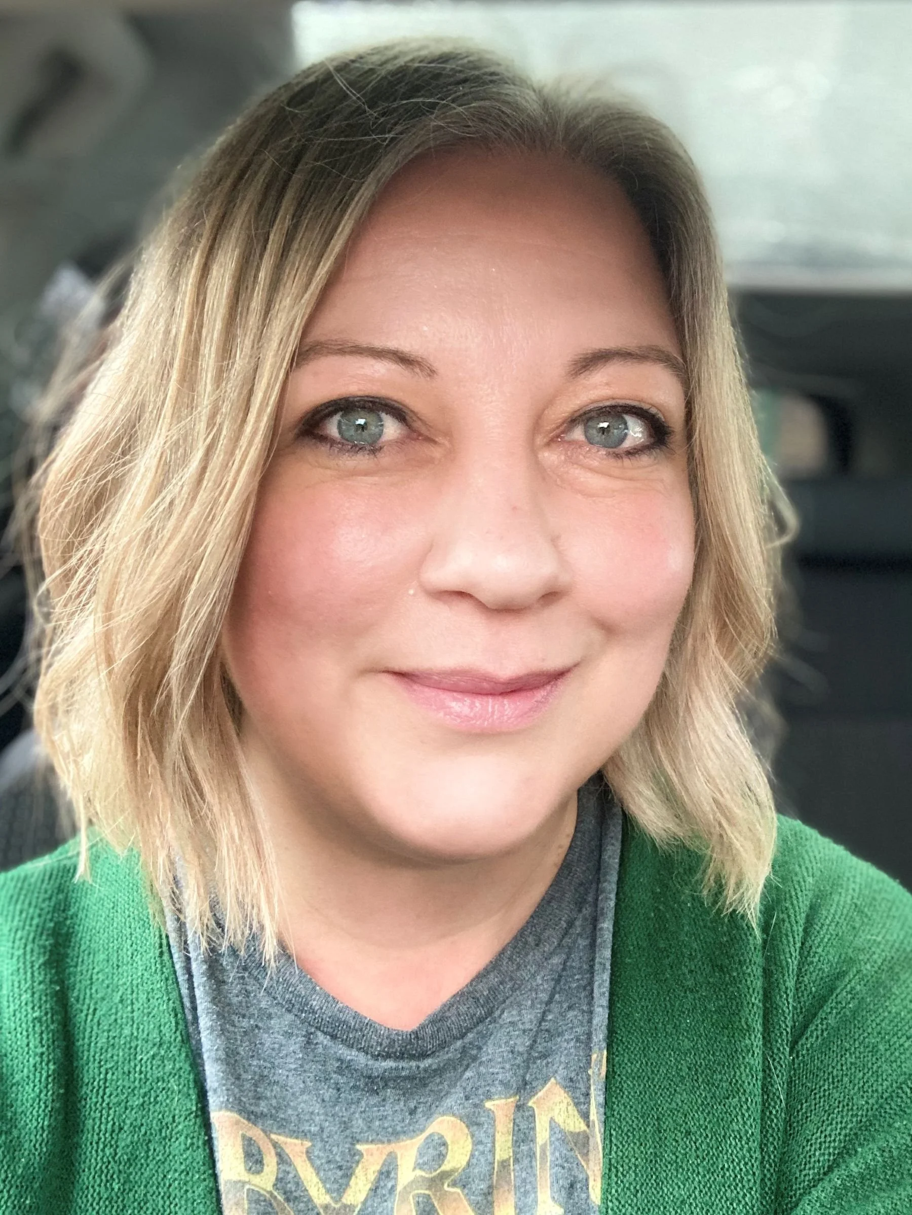 Hannah has shoulder-length blonde-grey hair and blue eyes with black eyeliner. She is smiling slightly and wearing a green cardigan over a grey T-shirt.