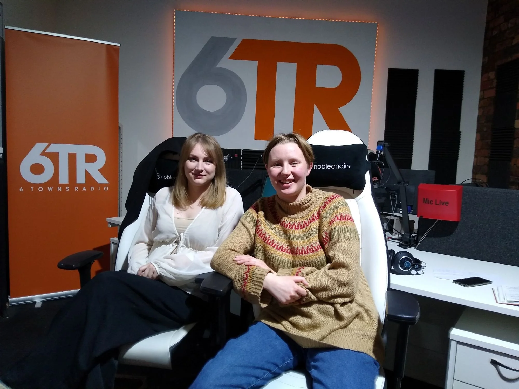 2 white women sit in the 6 Towns Radio studio smiling at the camera.