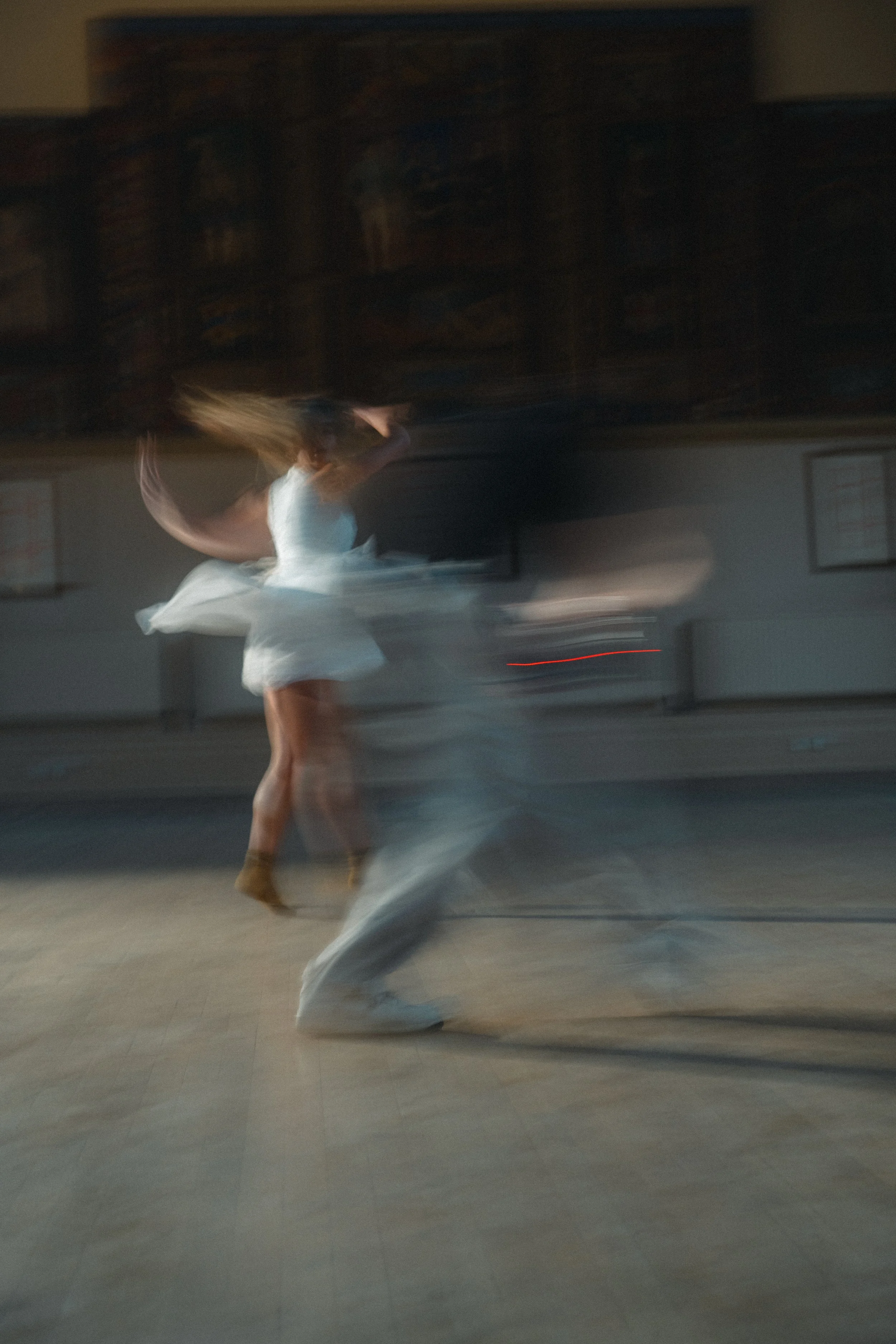 A woman in a white dress dancing with a man in a gray suit in an indoor space, captured with motion blur.